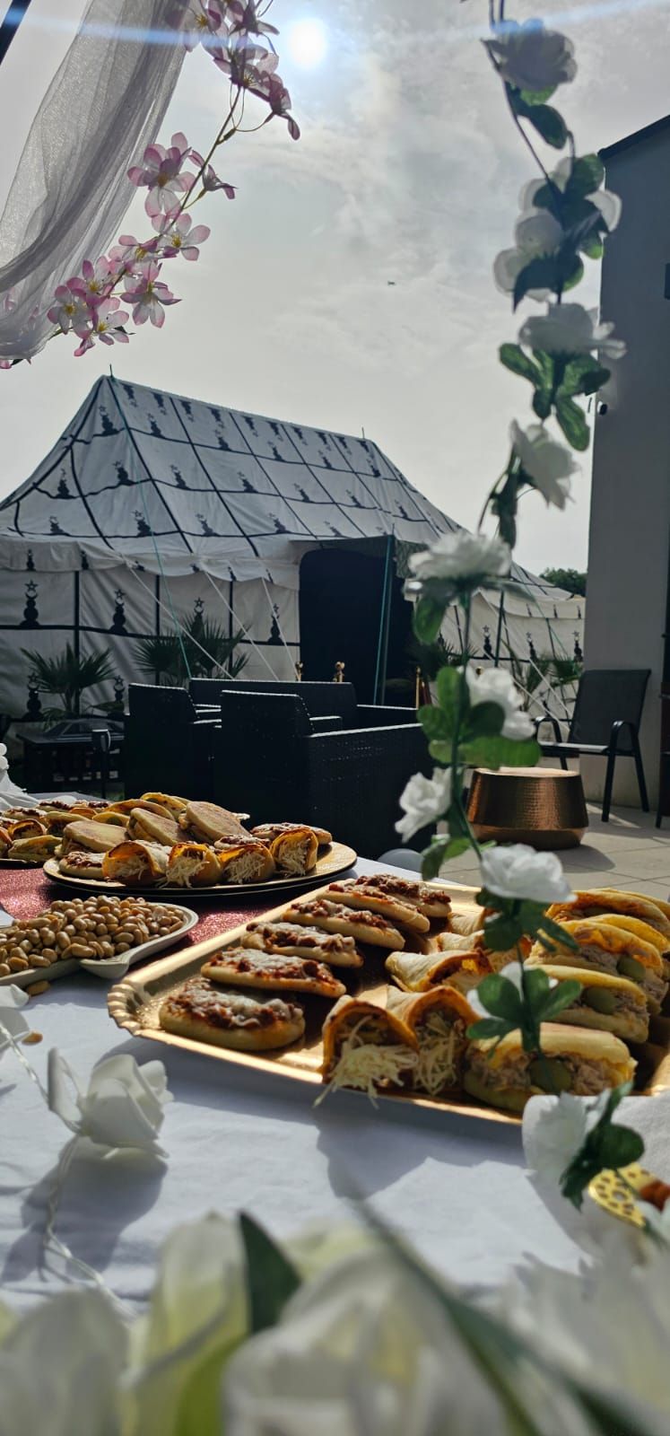 Une table garnie d'assiettes de nourriture et de fleurs avec une tente berbère en arrière-plan.