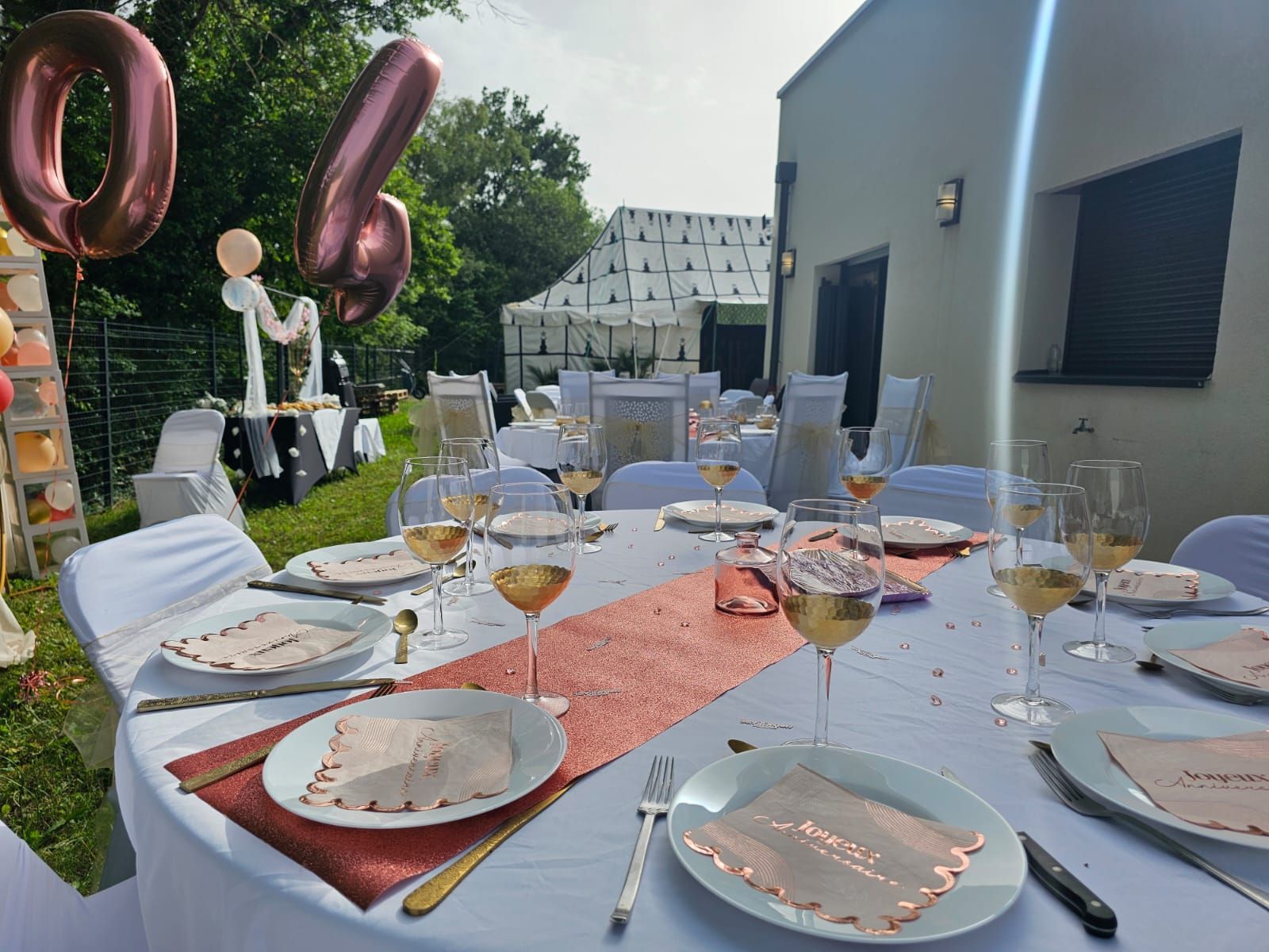 Une table dressée pour une fête avec des assiettes, des verres de vin et des ballons.