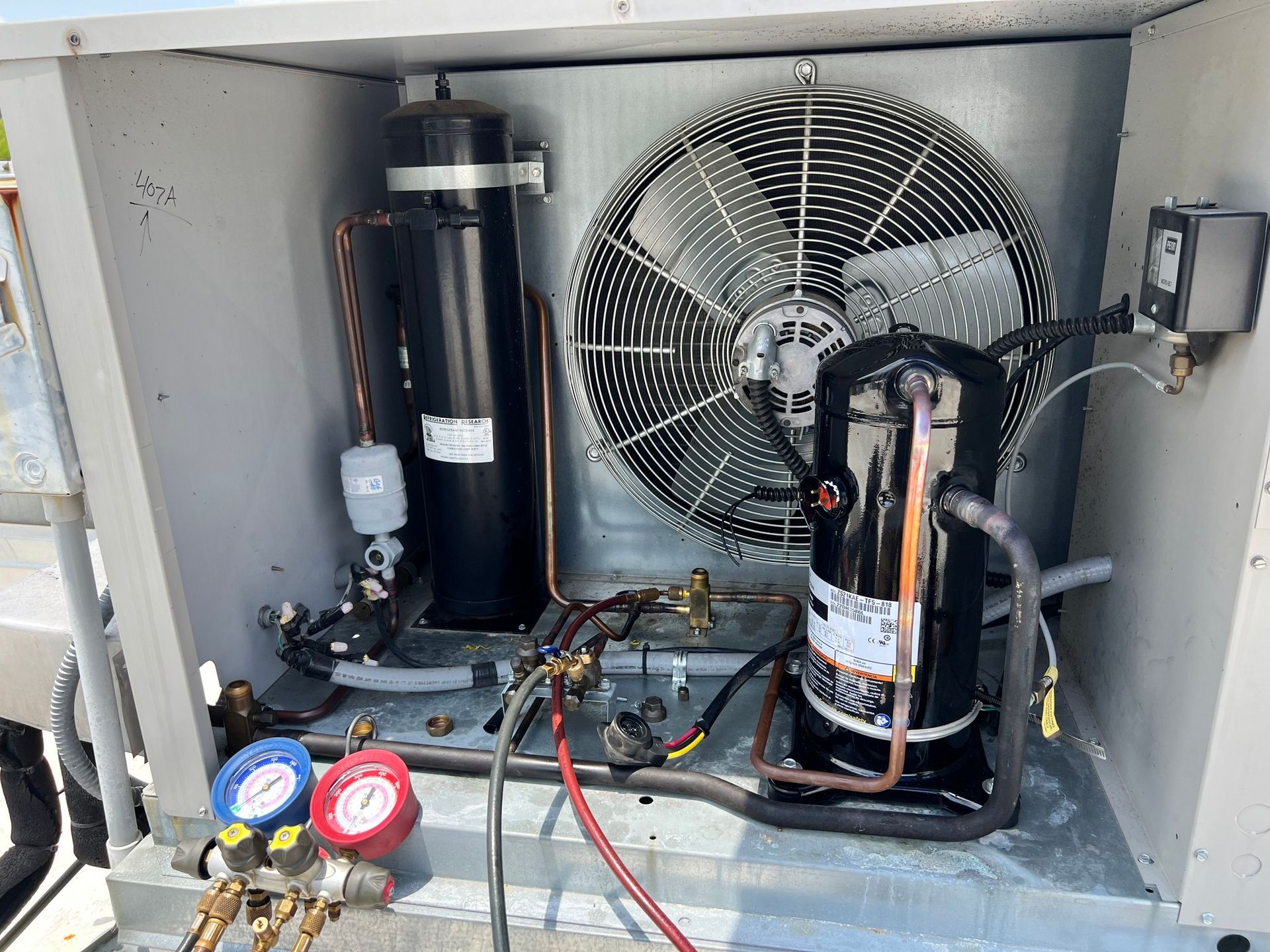 Inside view of an air conditioning unit with a fan, compressor, and gauges for maintenance.