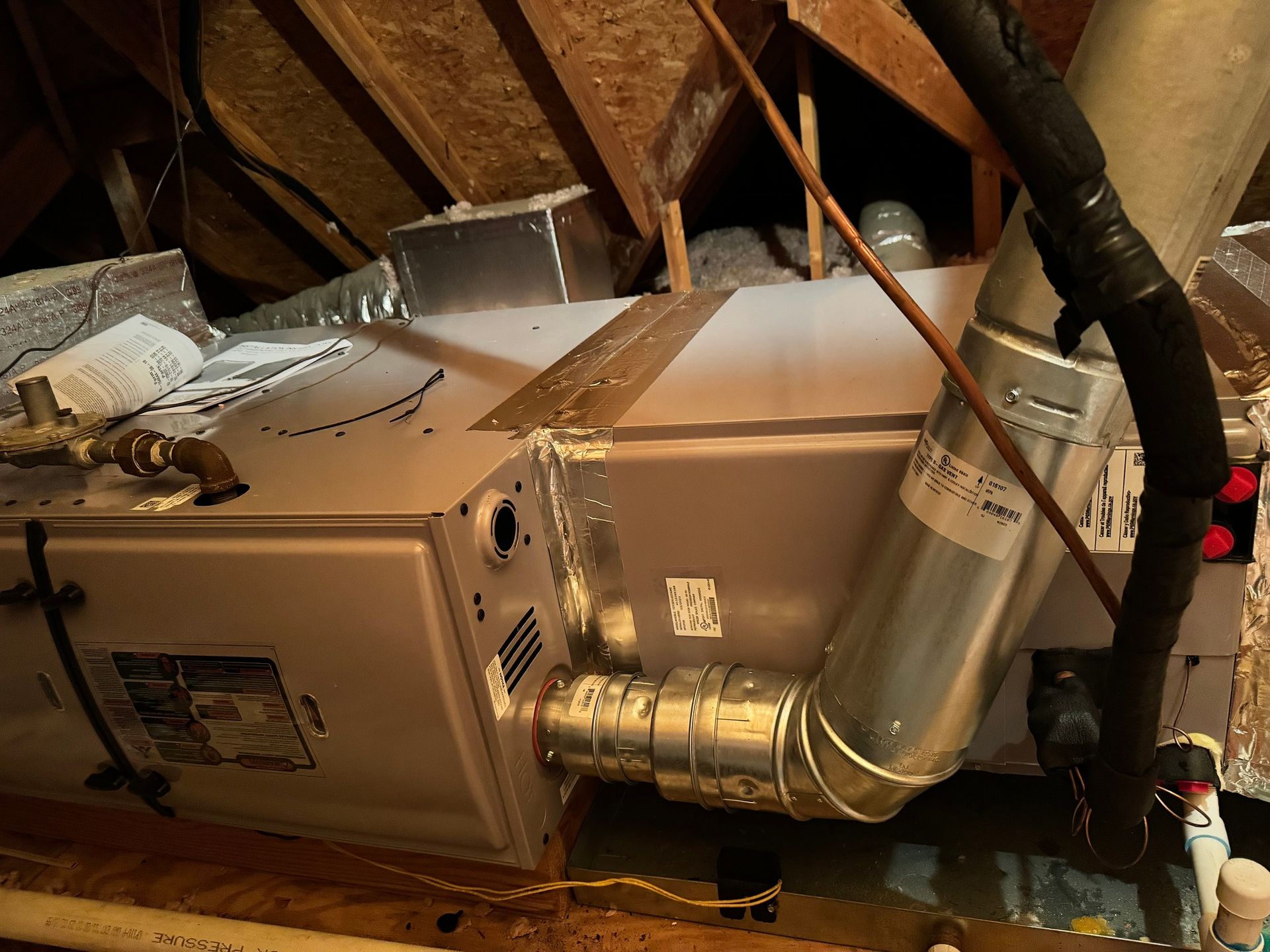 HVAC unit in an attic with ductwork, plumbing, and wooden supports visible.
