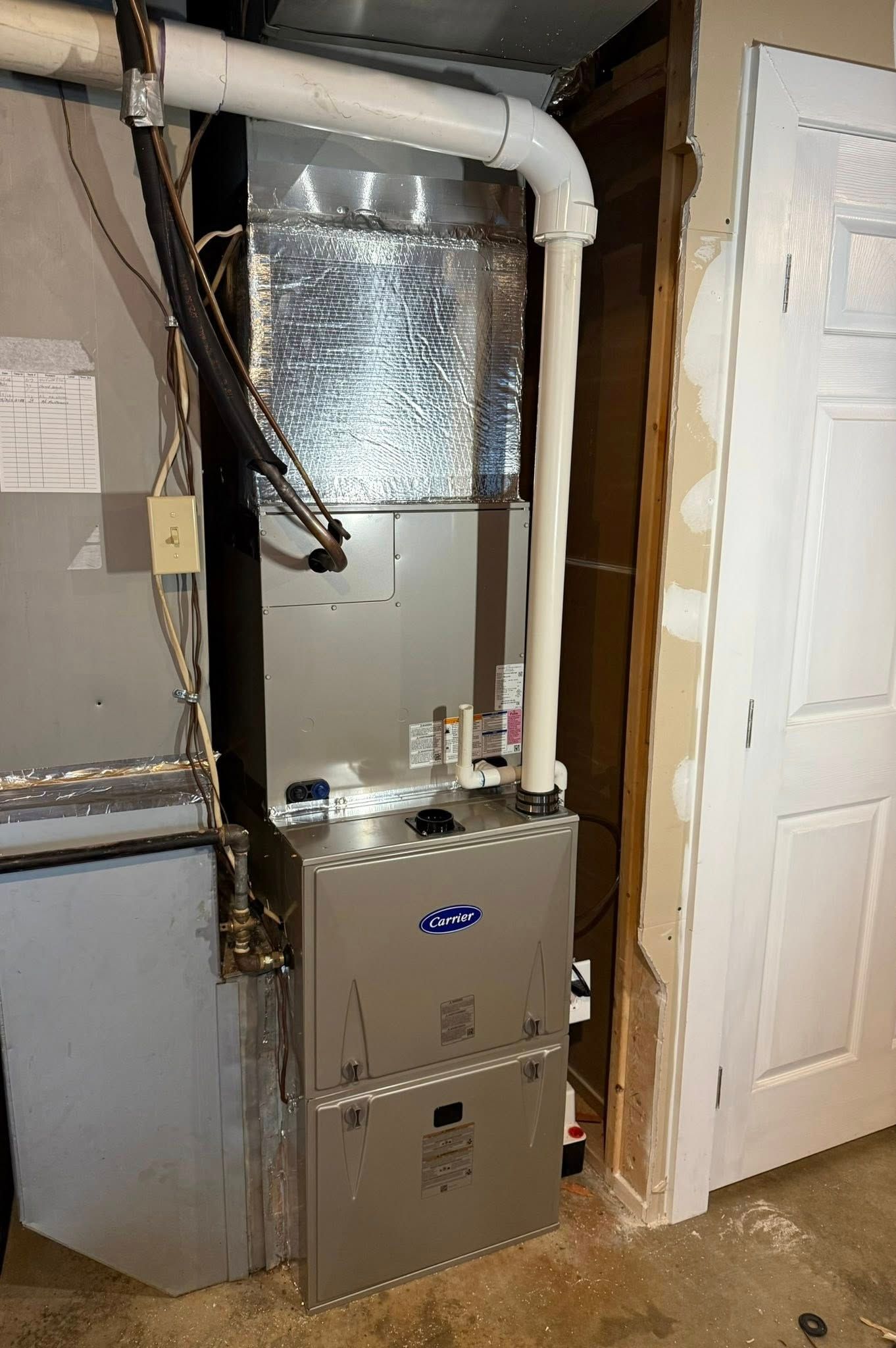 HVAC unit in a basement. Silver metal furnace with ductwork and a white door in the background.