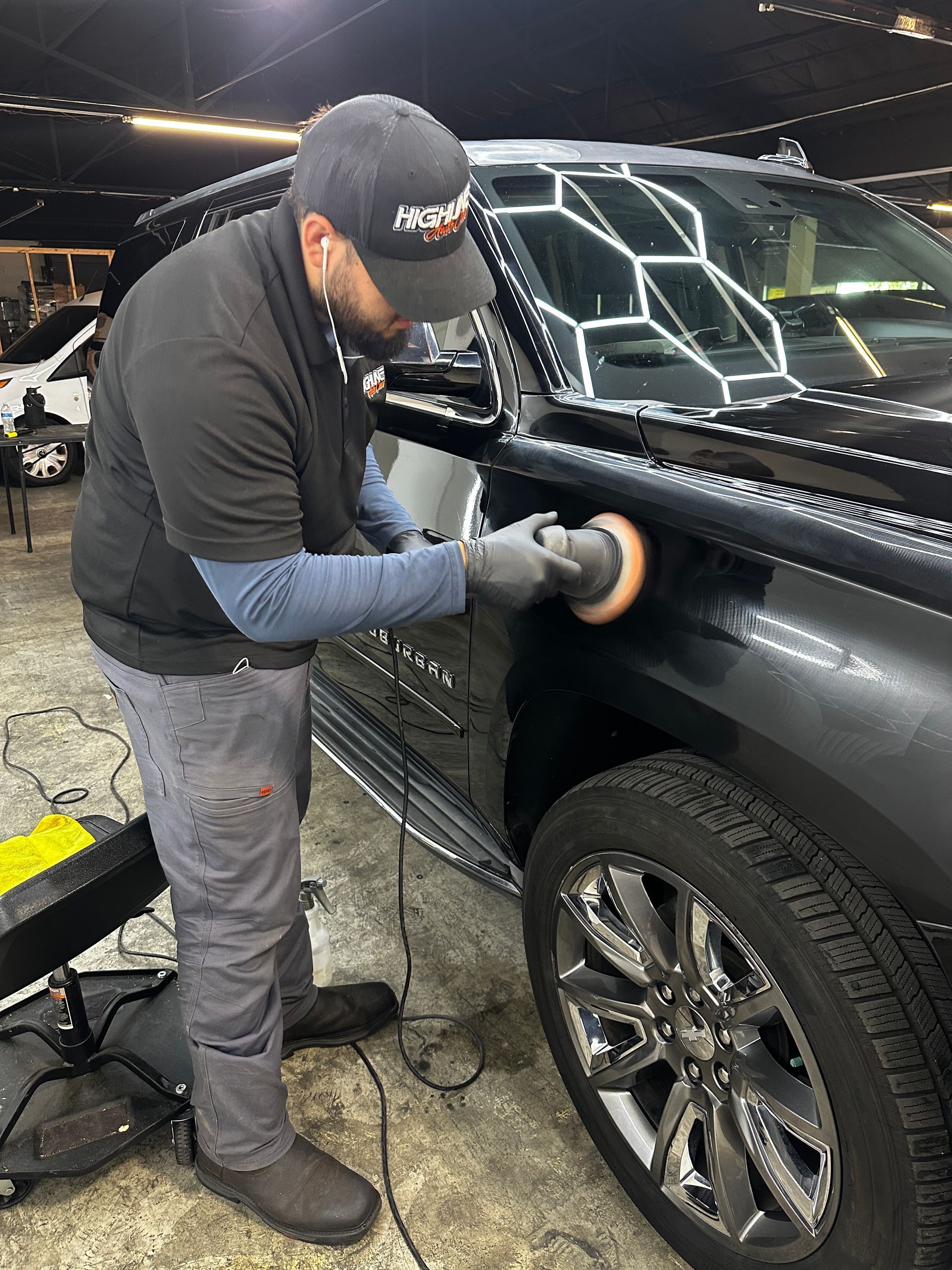 Person polishes a black SUV with a buffing machine inside a well-lit garage.