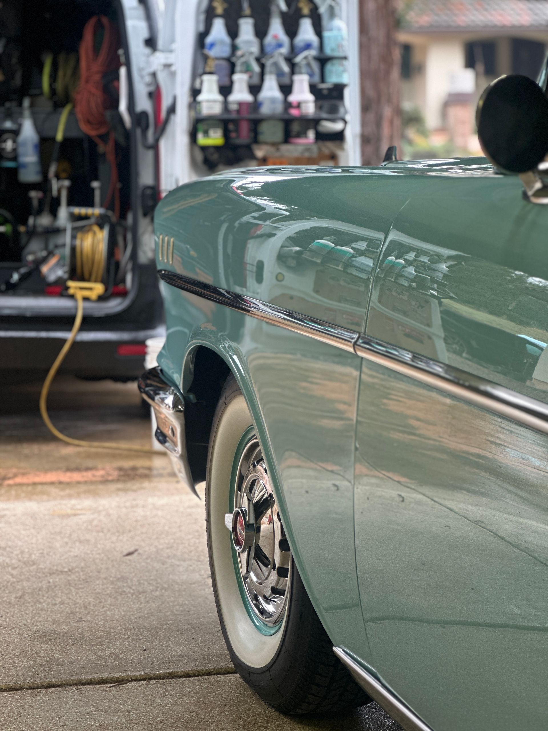 Classic teal car being detailed next to a van stocked with cleaning supplies.