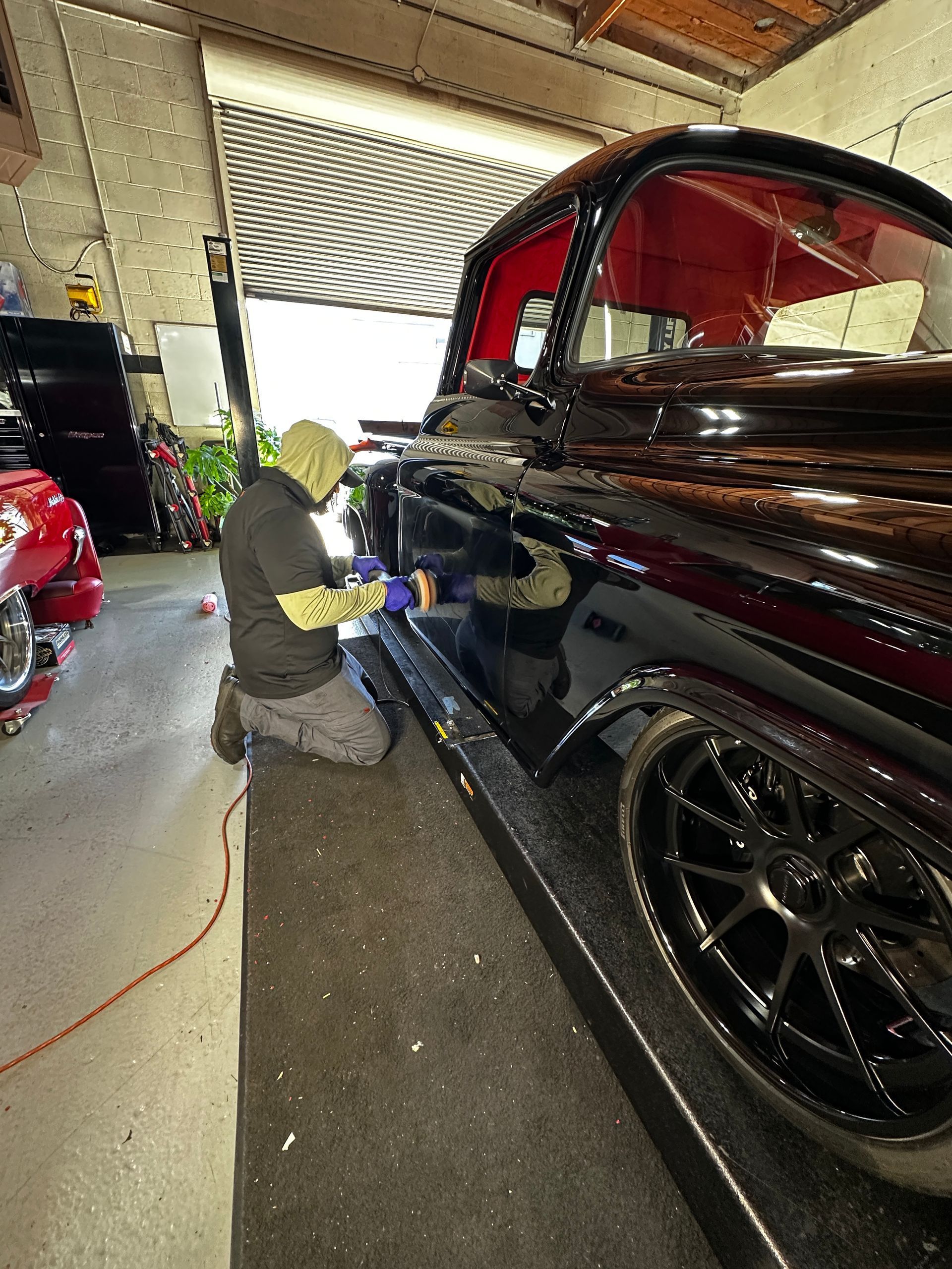 Man polishing a black classic truck in a garage; red interior, silver rims.