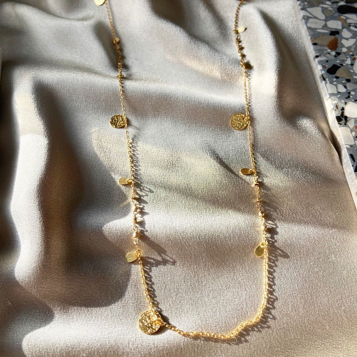 A gold necklace is laying on a white cloth