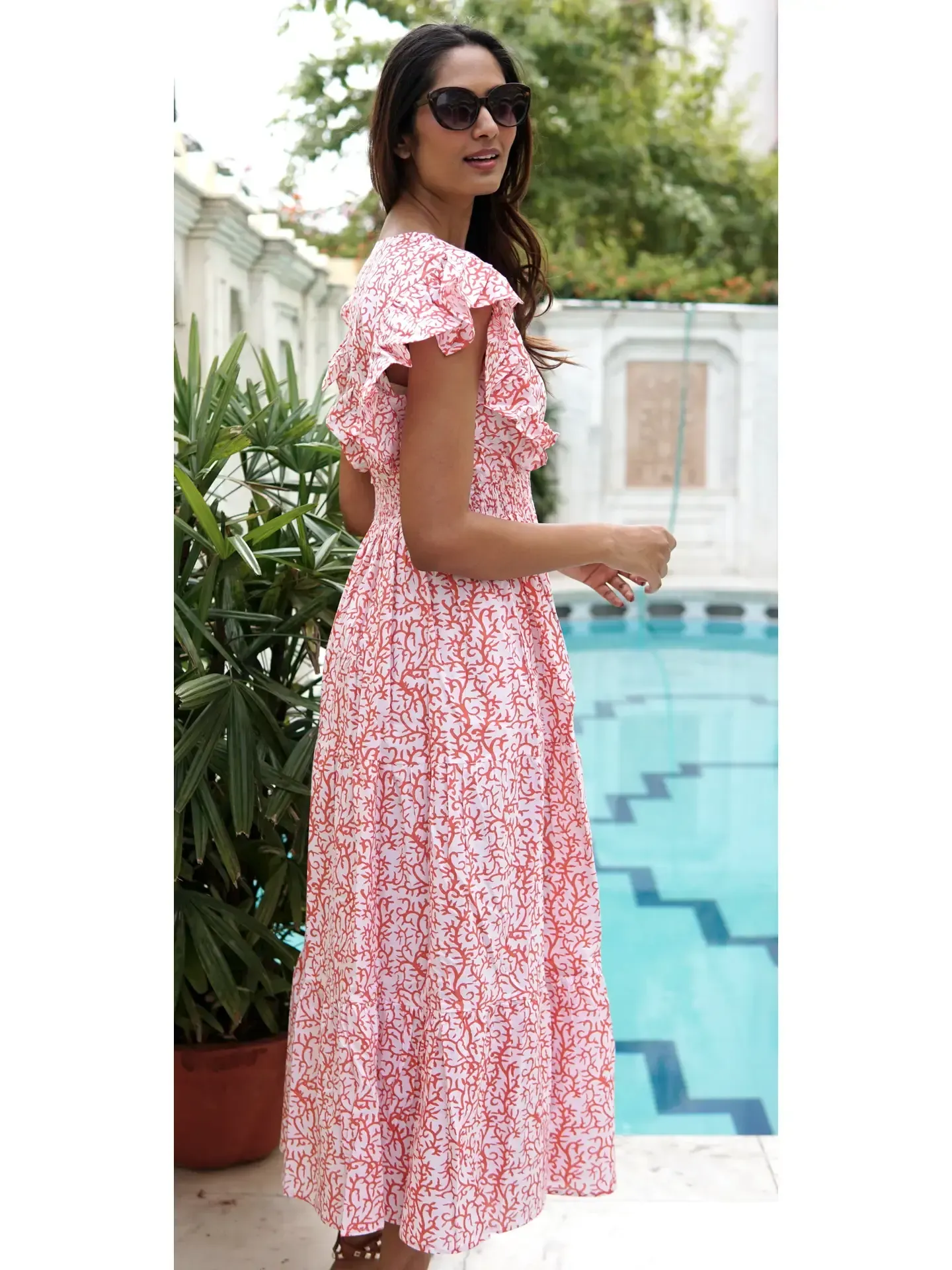 A woman in a pink and white dress is standing next to a pool.