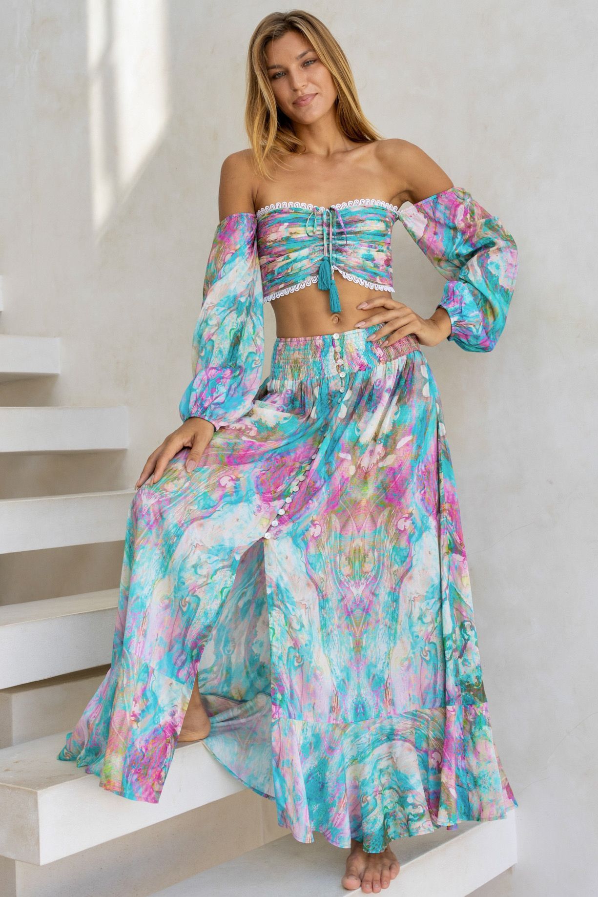 A woman is standing on a set of stairs wearing a crop top and a long skirt.