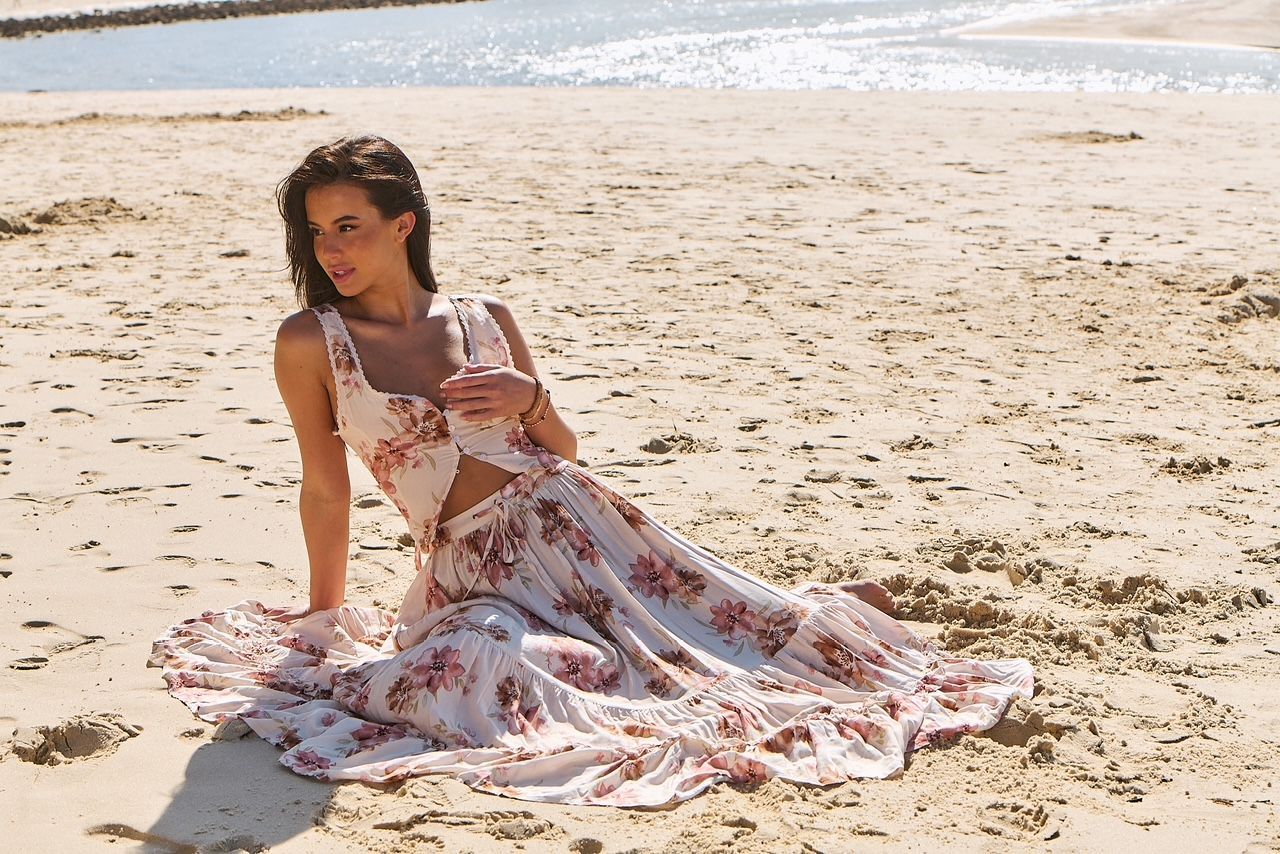 A woman in a long dress is sitting on the beach.