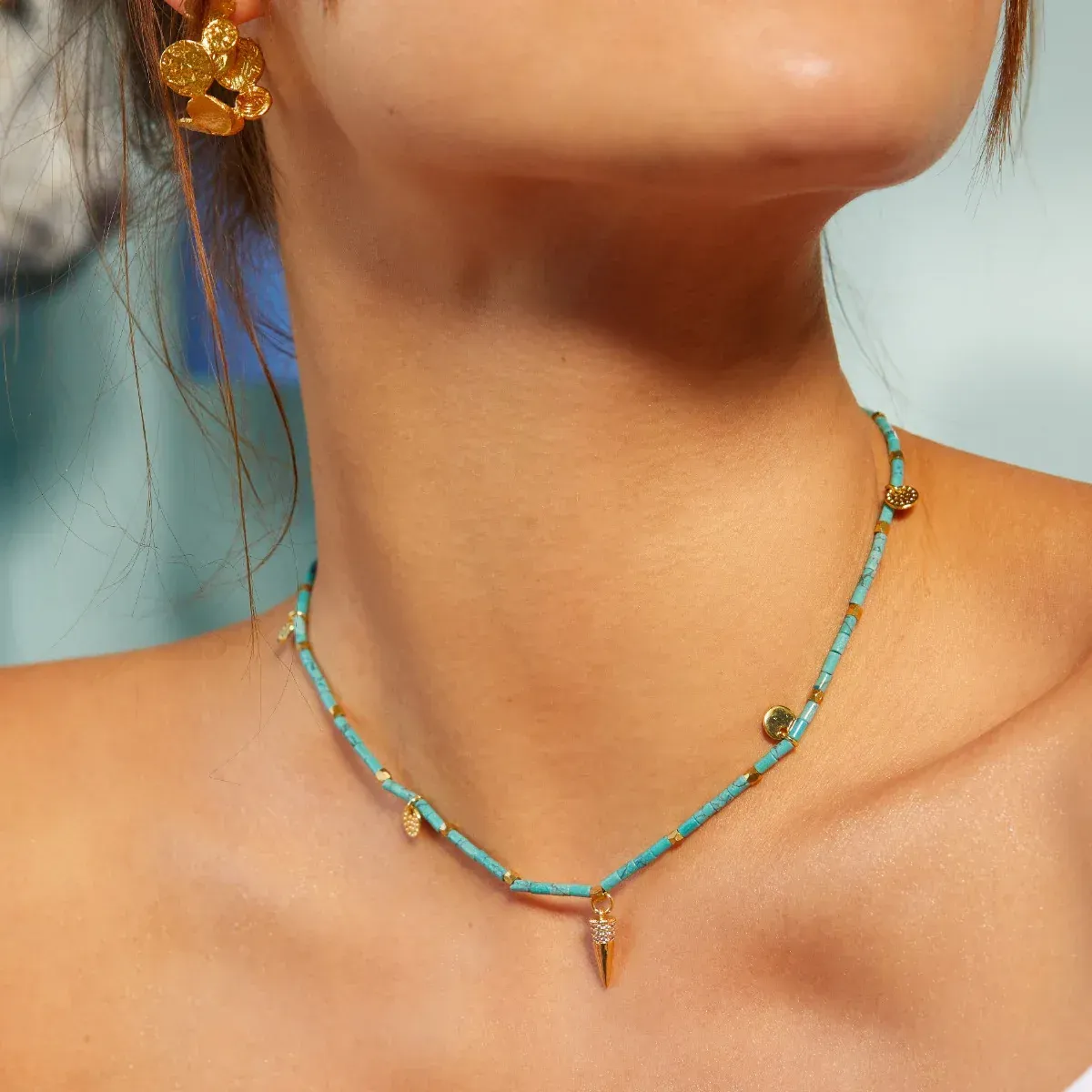 A woman wearing a turquoise necklace and gold earrings