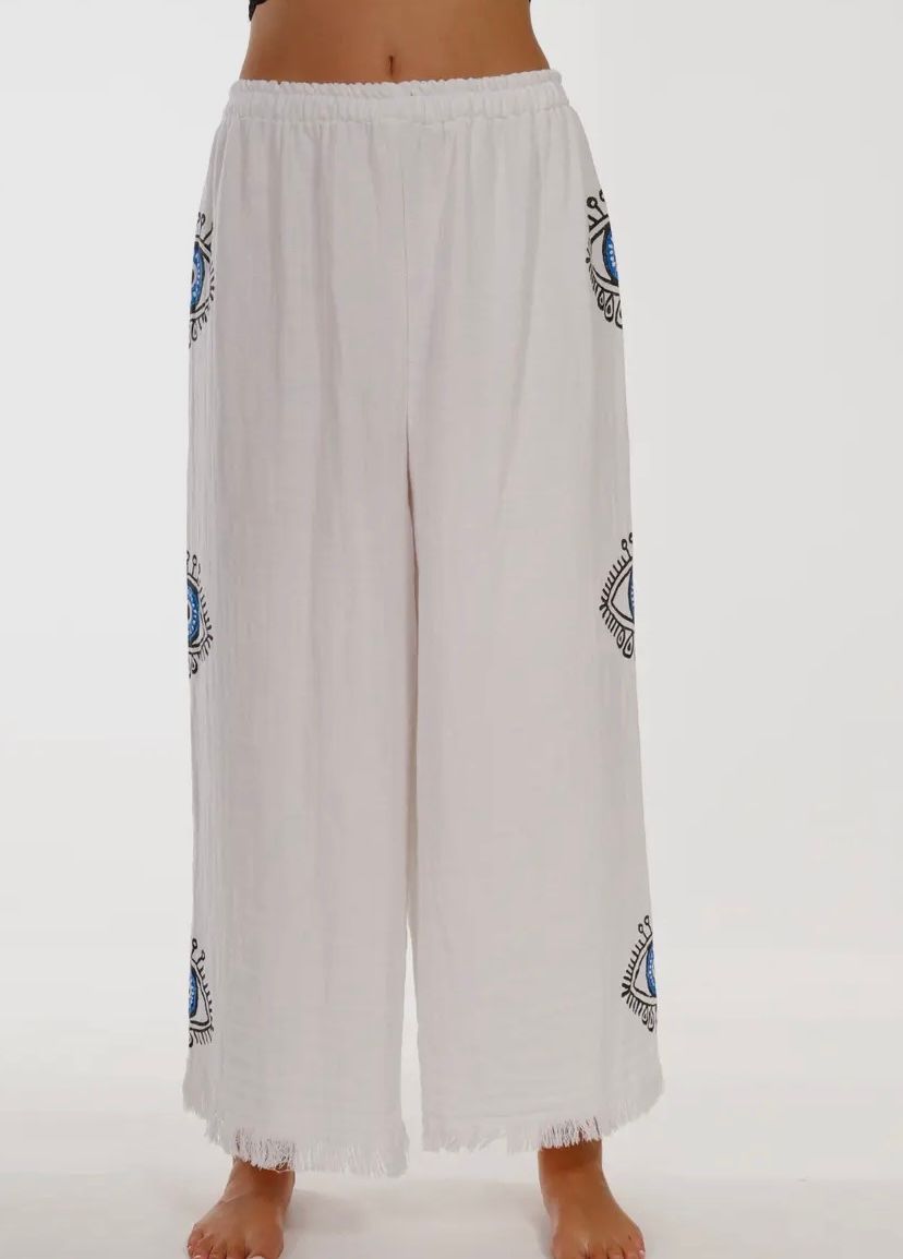 A woman is wearing a pair of white pants with blue embroidery
