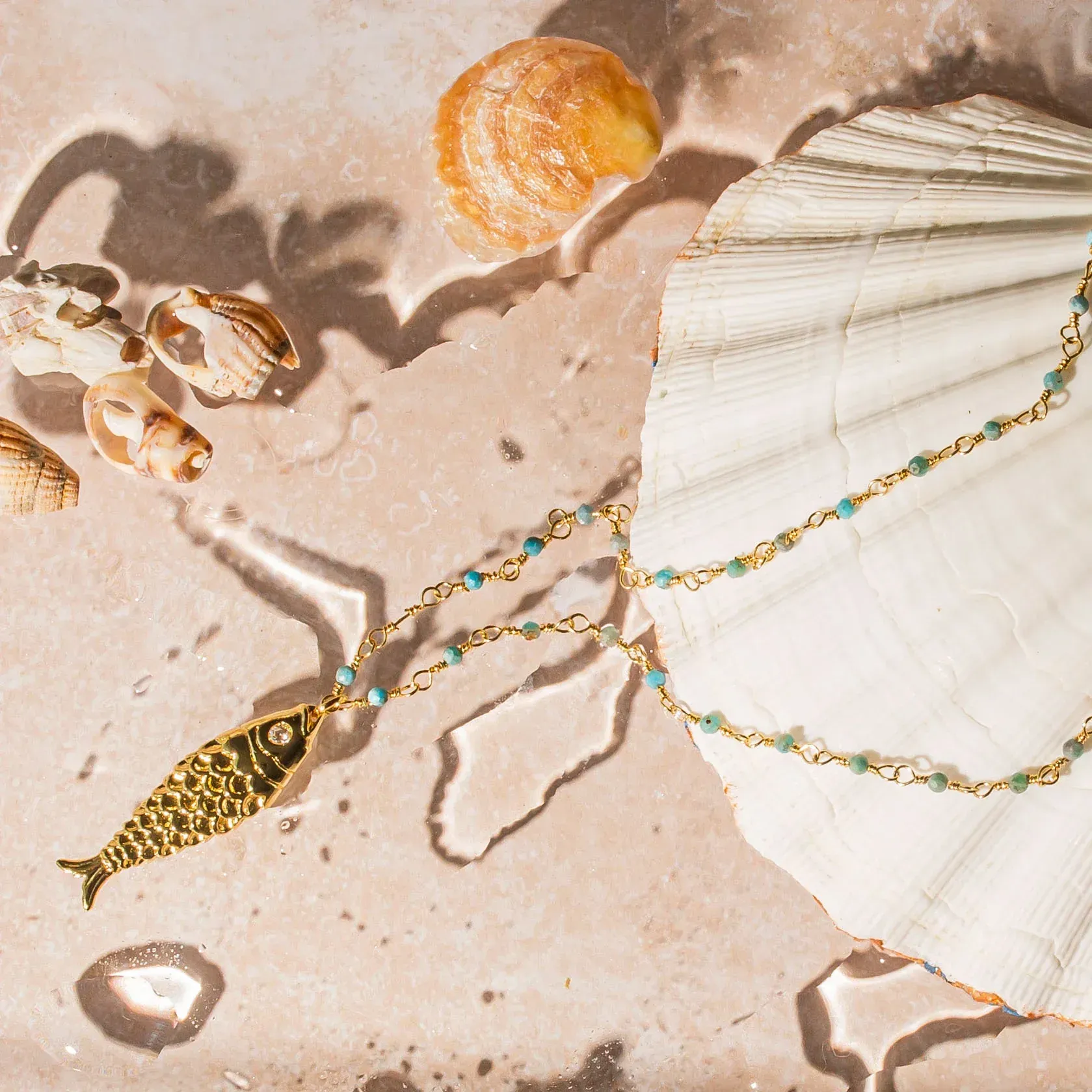 A necklace with a fish on it is sitting on a shell.