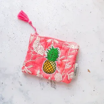 A pink purse with a pineapple on it is sitting on a table.