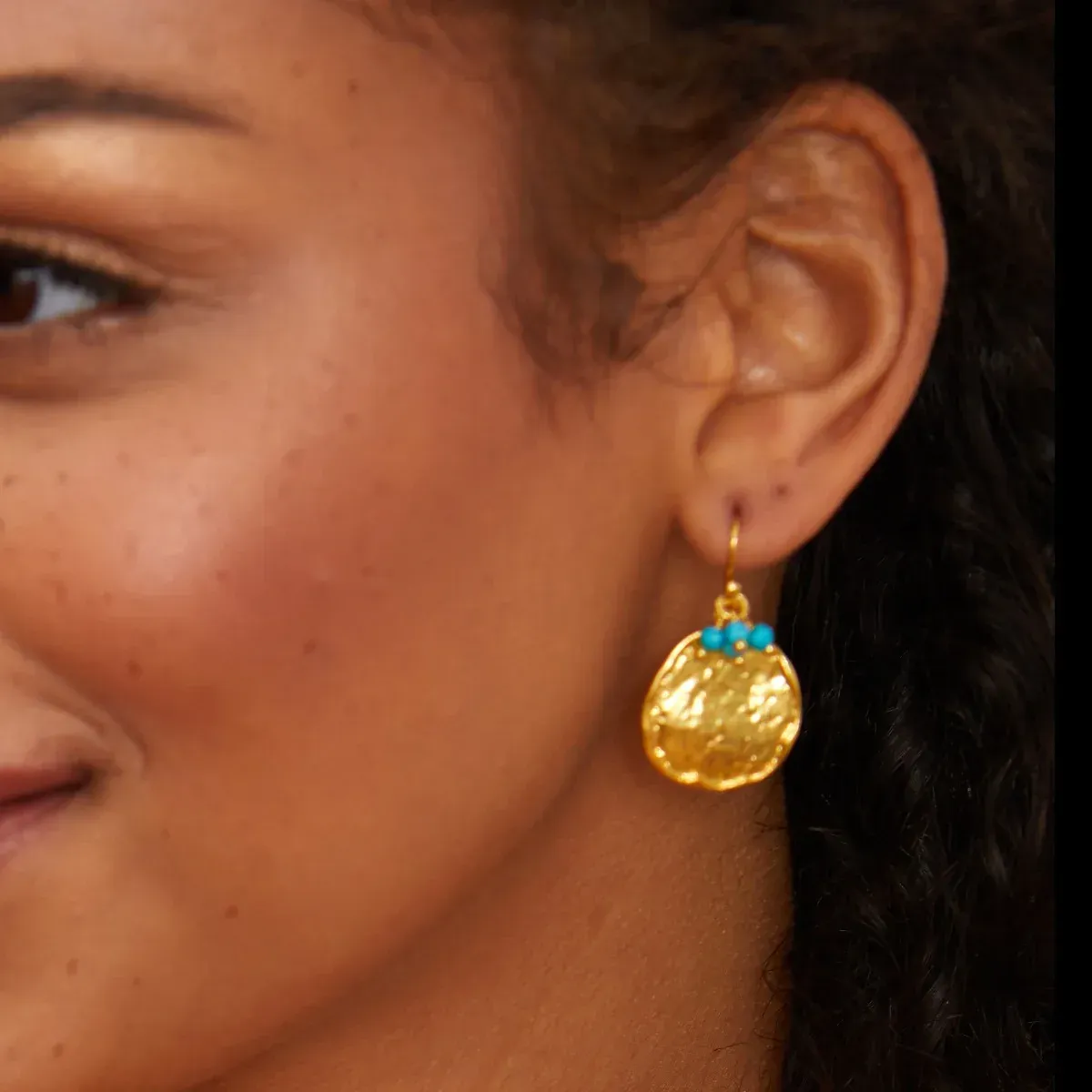 A woman wearing a pair of gold earrings with blue beads