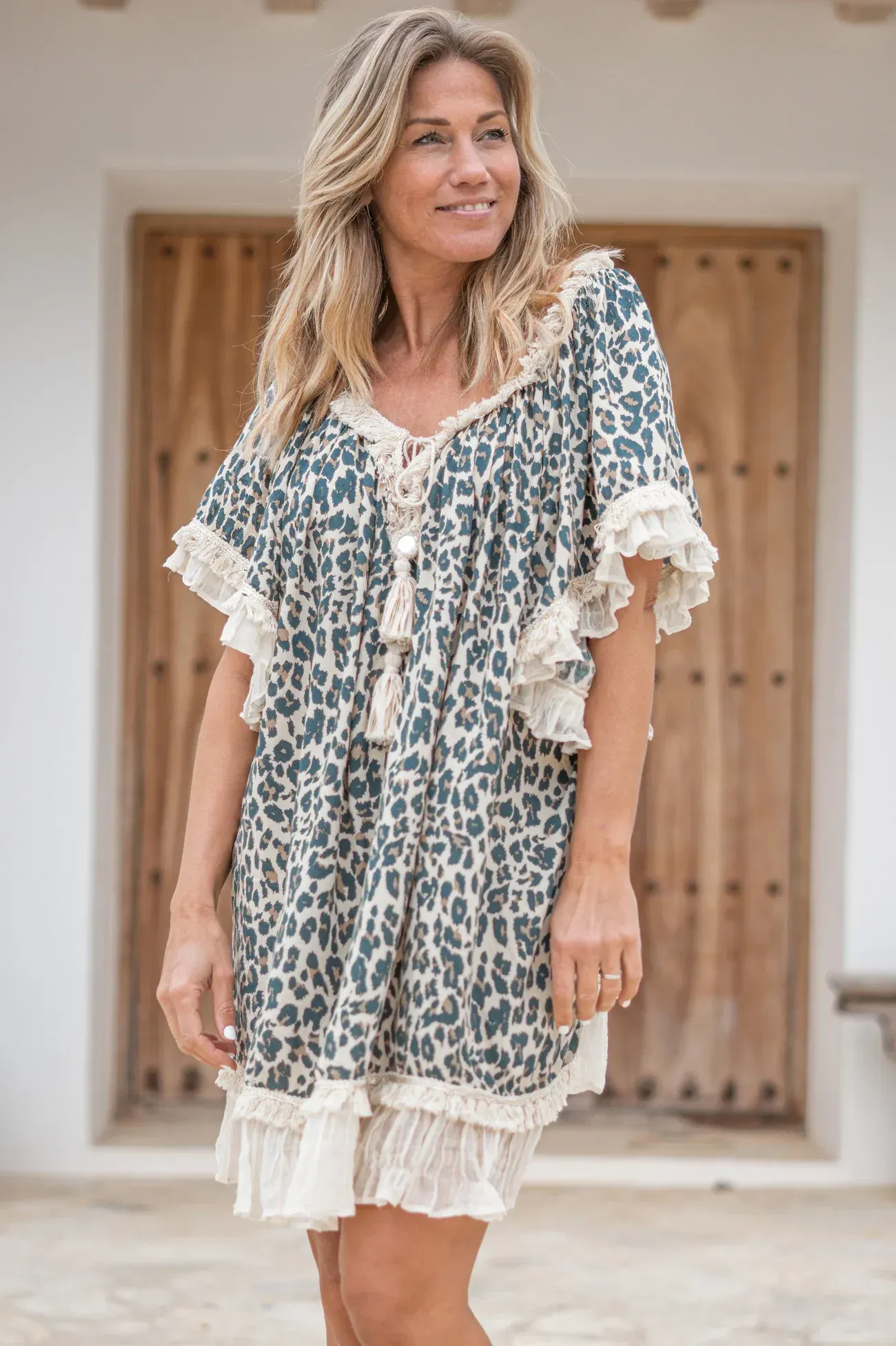 A woman in a leopard print dress is standing in front of a wooden door.
