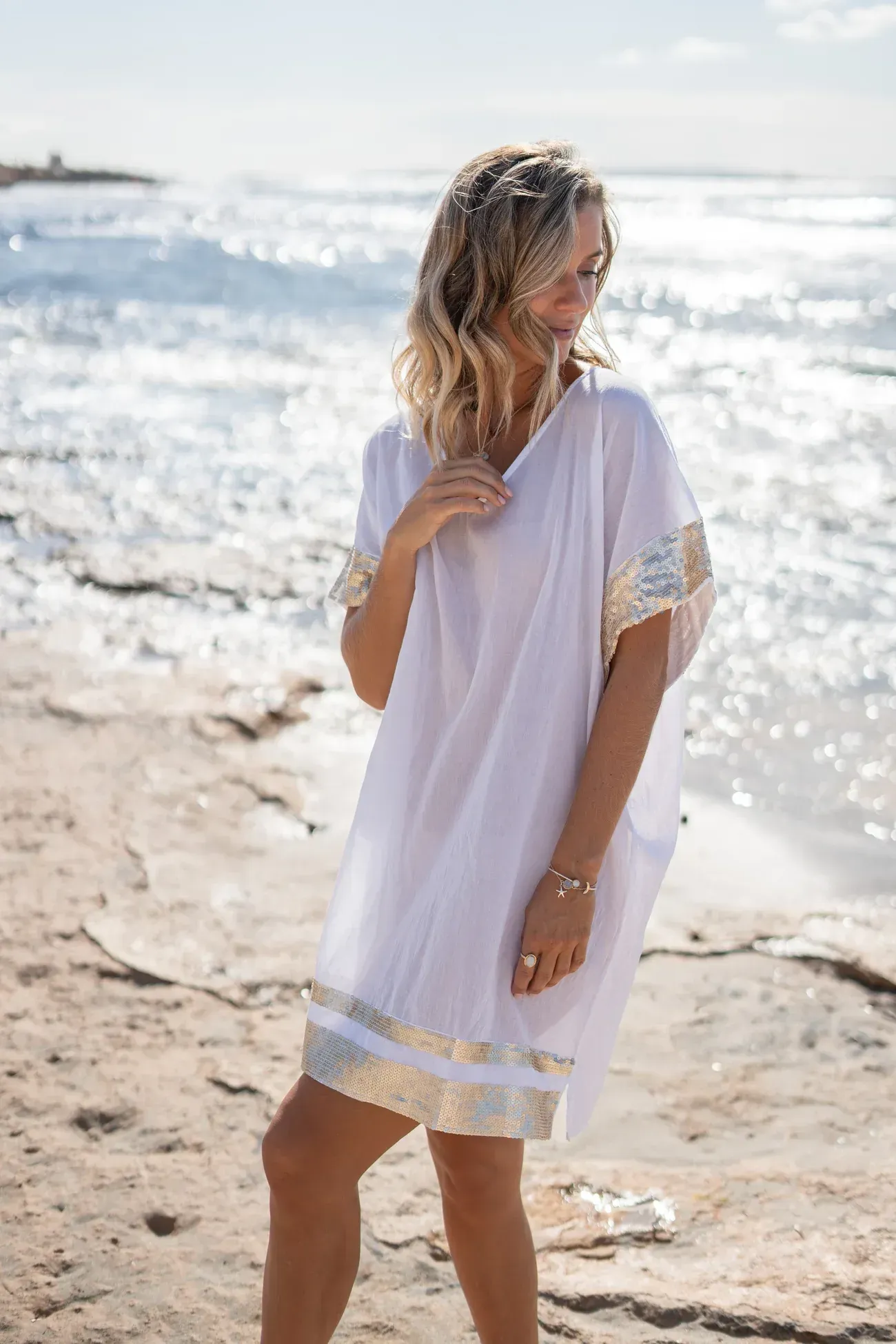 A woman in a white dress is standing on a beach.