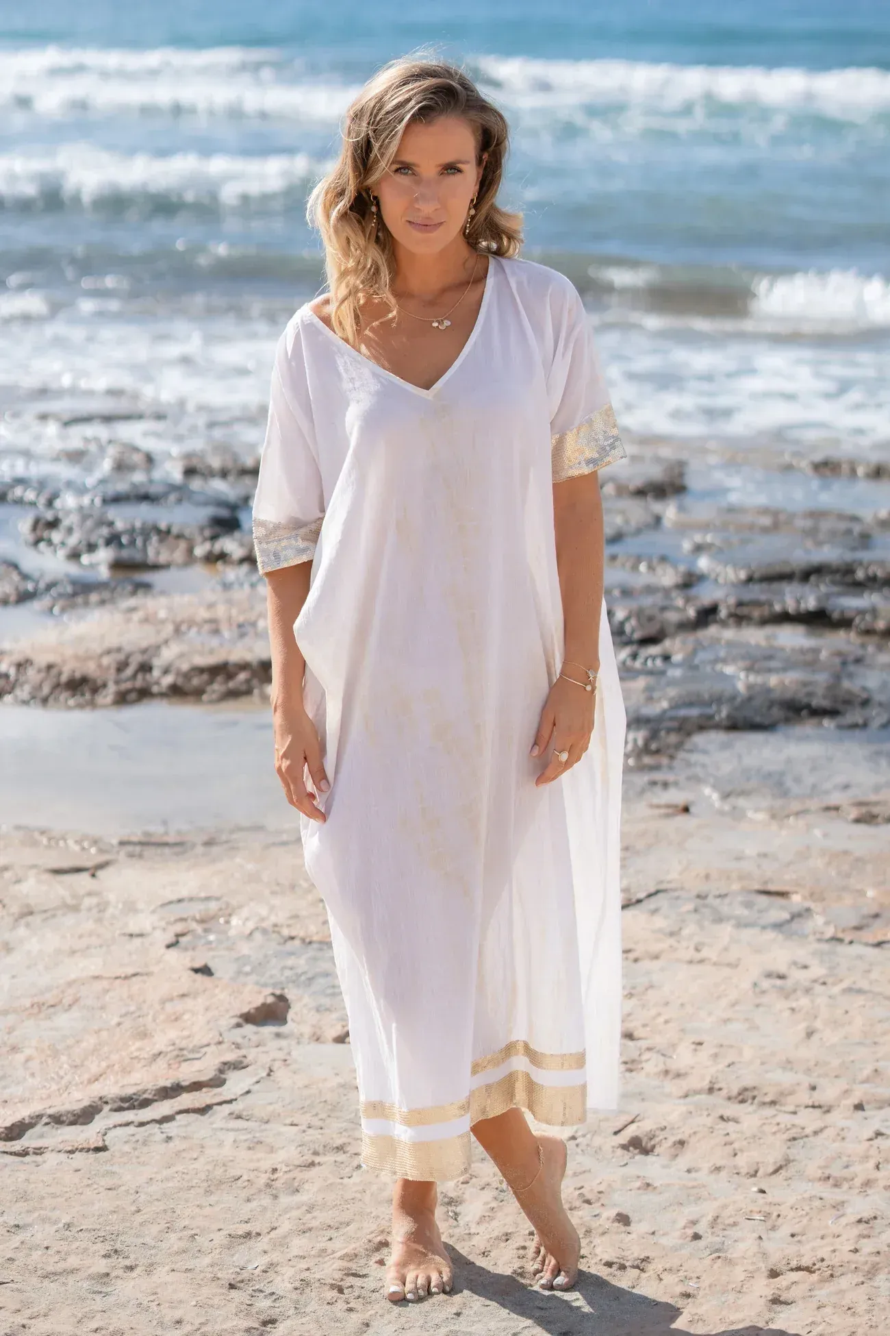 A woman in a white dress is standing on a beach.
