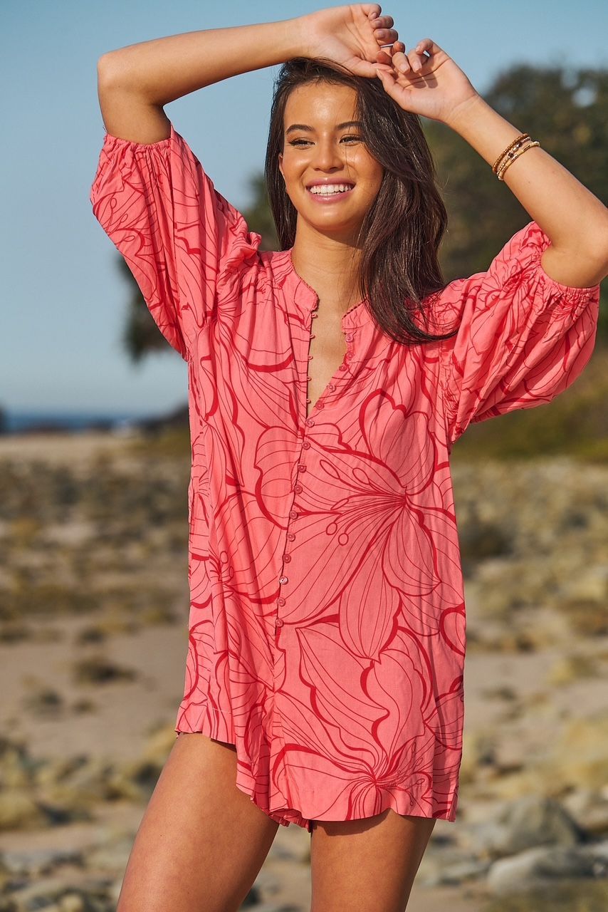 A woman in a pink dress is standing on a beach.