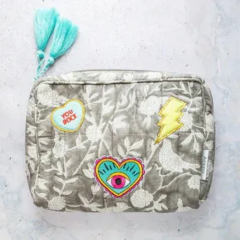A cosmetic bag with embroidered patches on it is sitting on a table.
