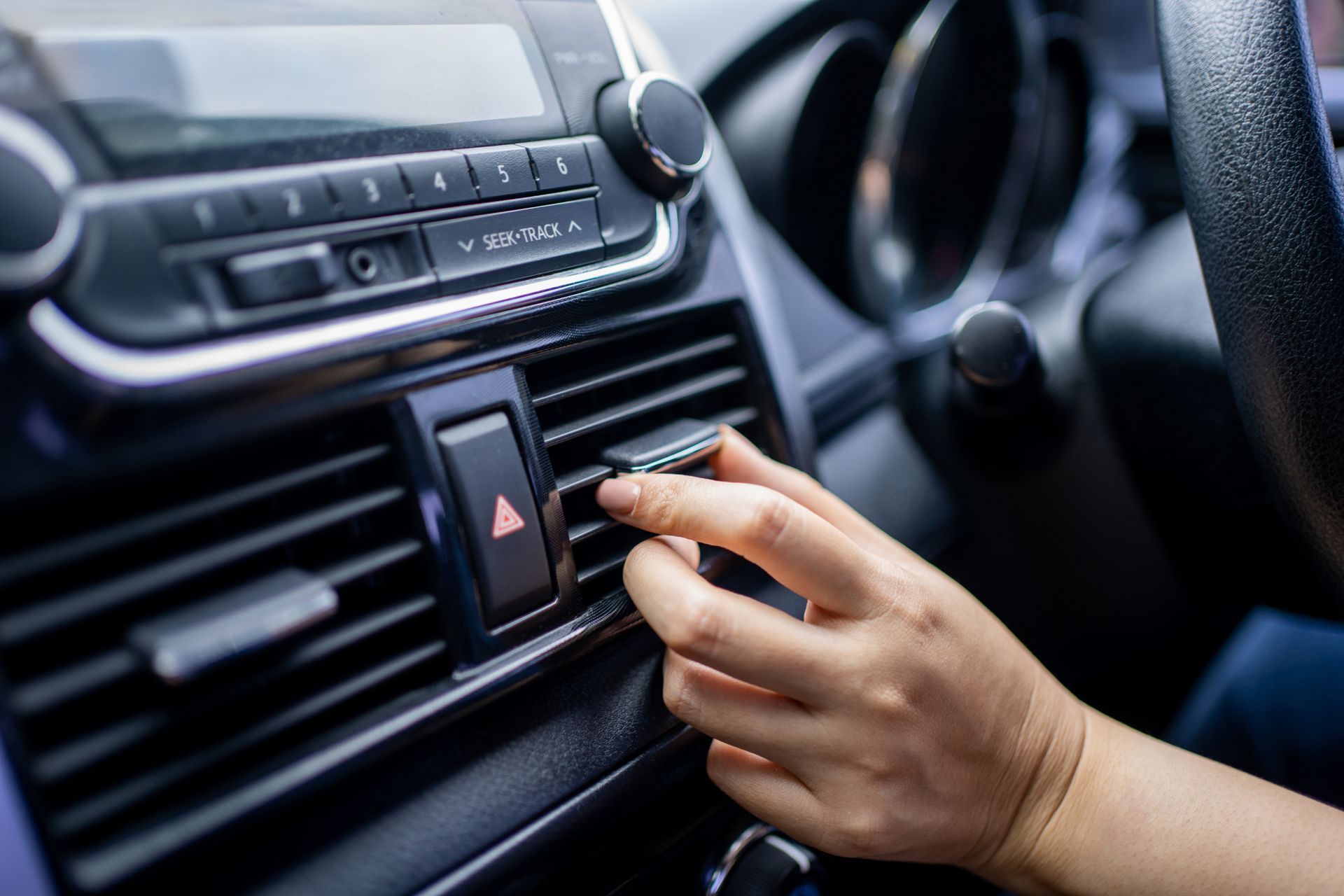 Hand turning a car dashboard air vent, with hazard button and radio controls visible