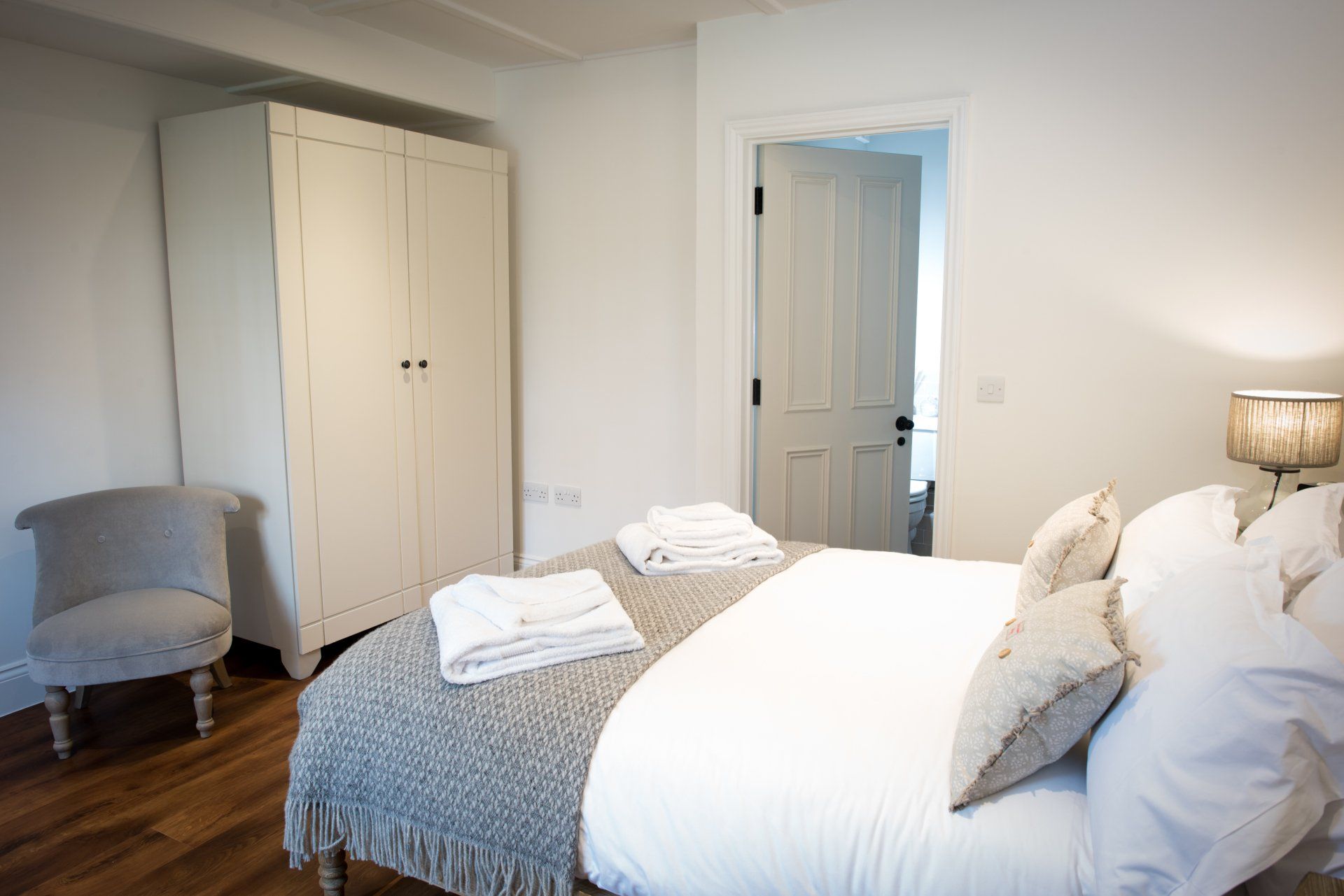 A bedroom with a bed , chair , lamp and wardrobe.