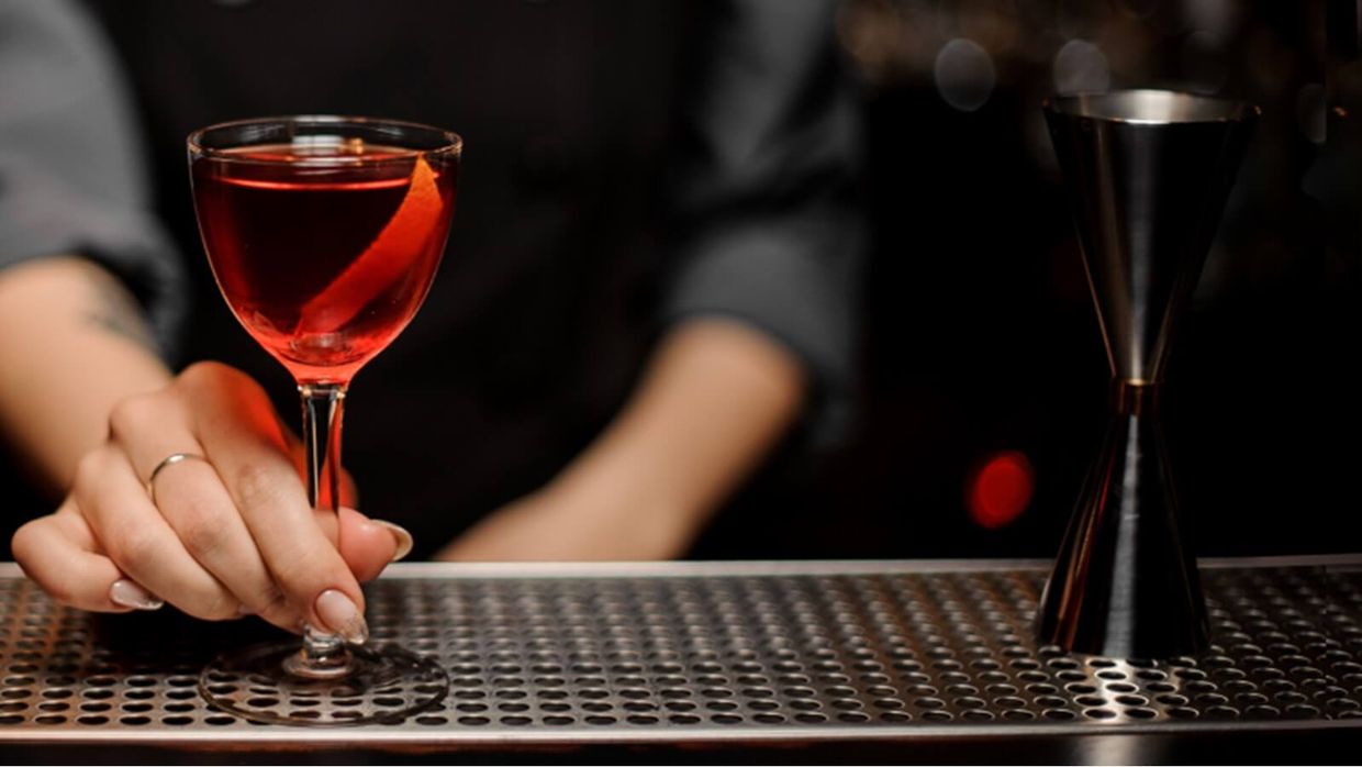 a bartender is holding a glass of red wine on a bar .