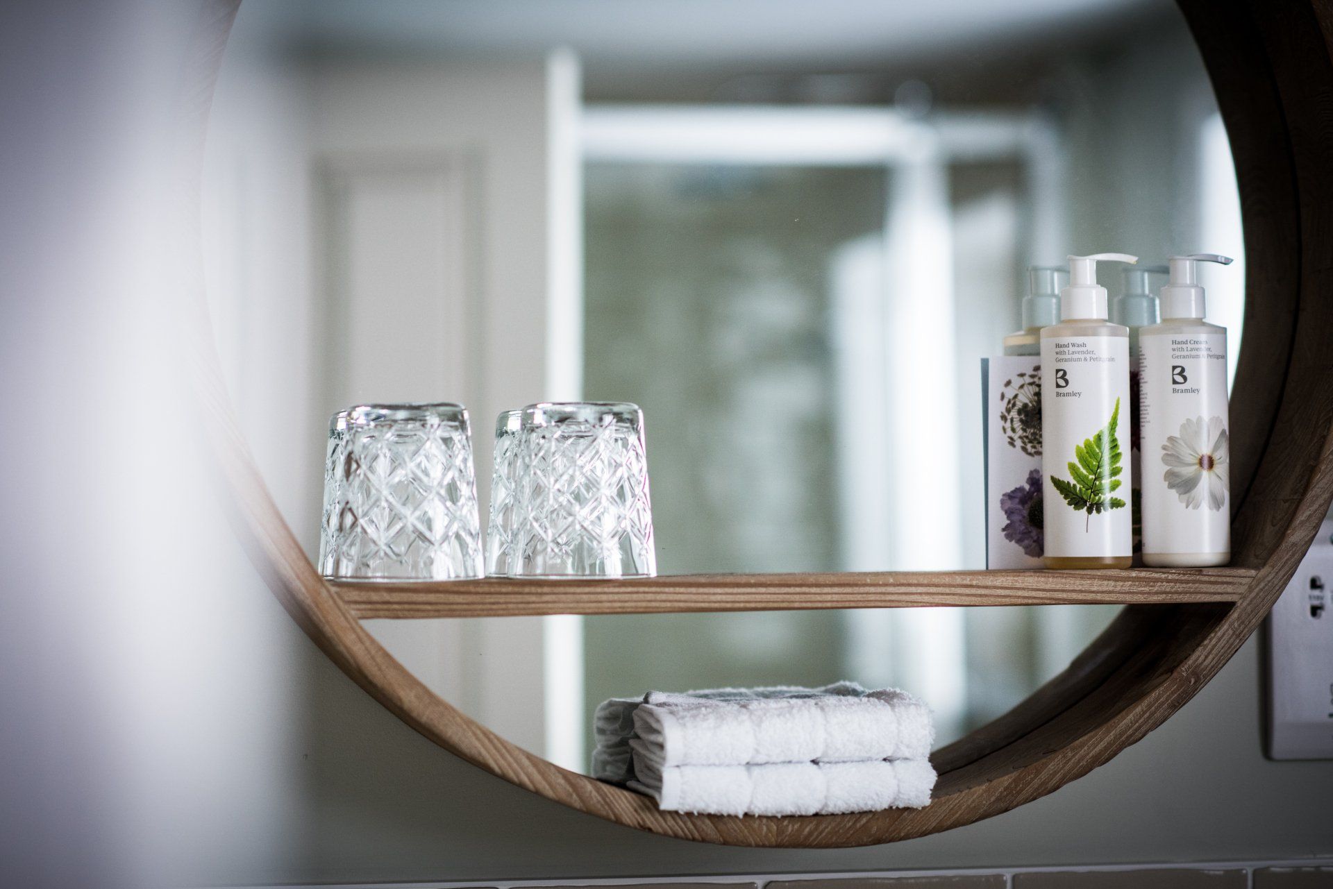 a bathroom mirror with a wooden shelf with bottles and glasses on it .