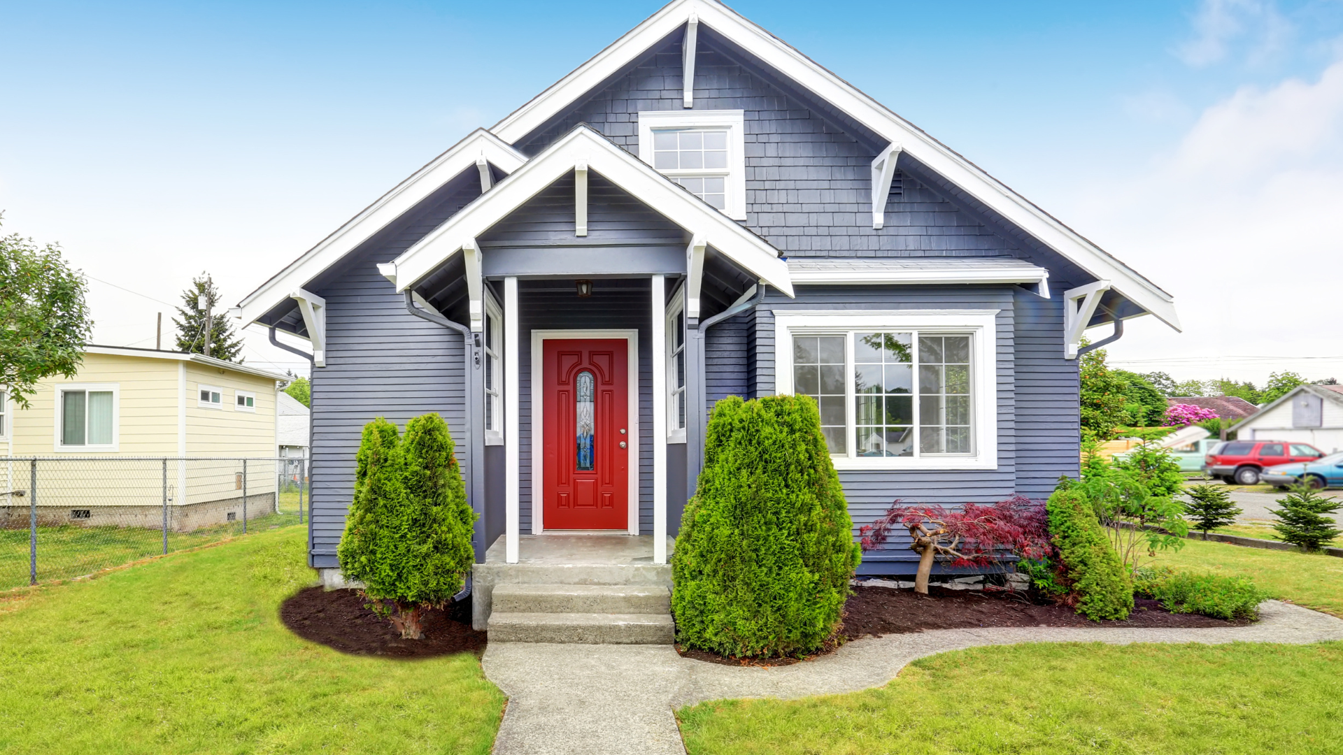 Blue house with red door, small porch, and green landscaping.