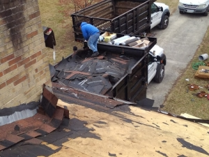 A person loading roofing debris into a truck on a roof. A brick wall is next to it.