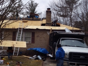 Roofers working on a house; truck parked in front. Construction debris and ladders on the ground.