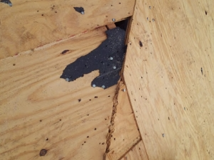 Plywood corner with dark, textured material filling a gap.