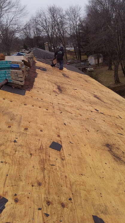 Person walking on a wooden roof; stacks of wood and supplies visible.