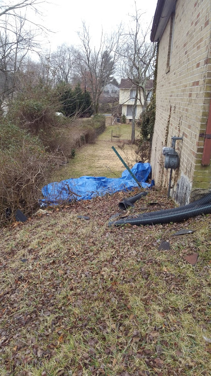 Backyard with a blue tarp covering leaves, brown grass, and a brick house.