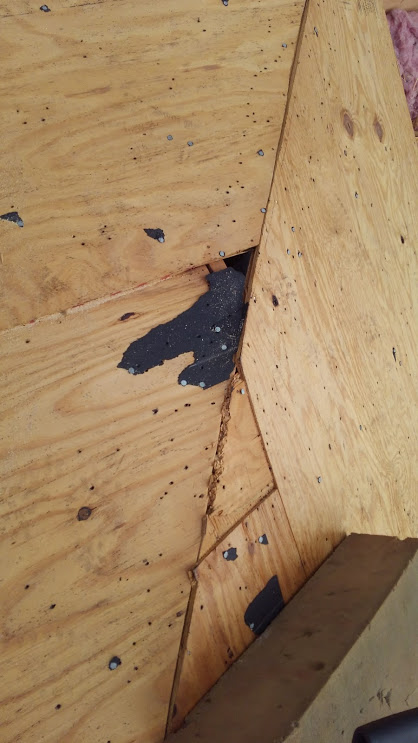 Plywood roof structure with a dark spot, possibly a hole, in the corner.