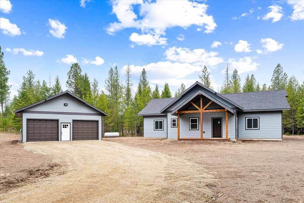 A large house with a garage in the middle of a dirt field surrounded by trees.