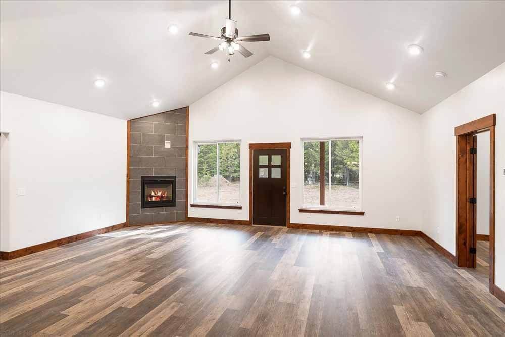 An empty living room with hardwood floors, a fireplace, and a ceiling fan.