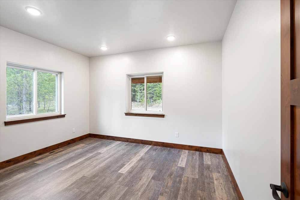An empty bedroom with hardwood floors and two windows.