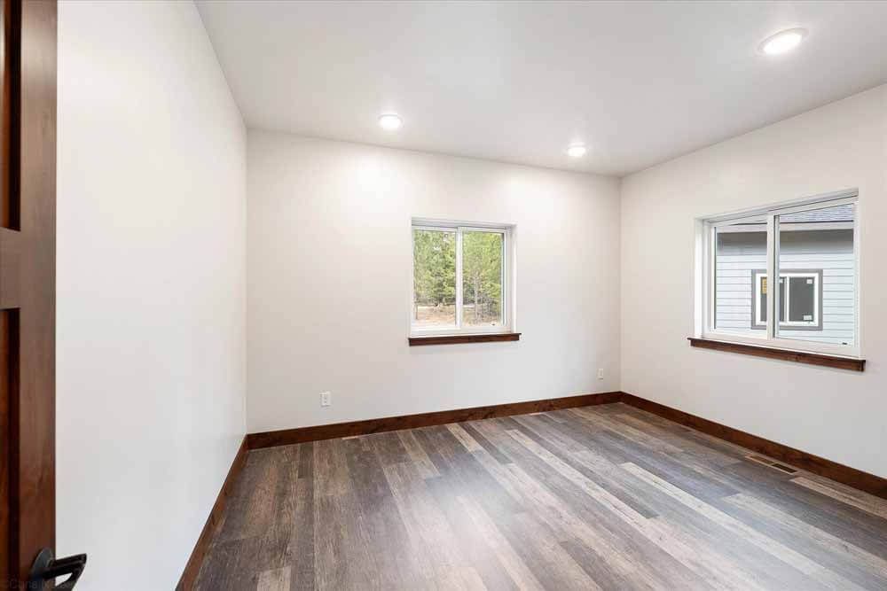 An empty room with hardwood floors and two windows.