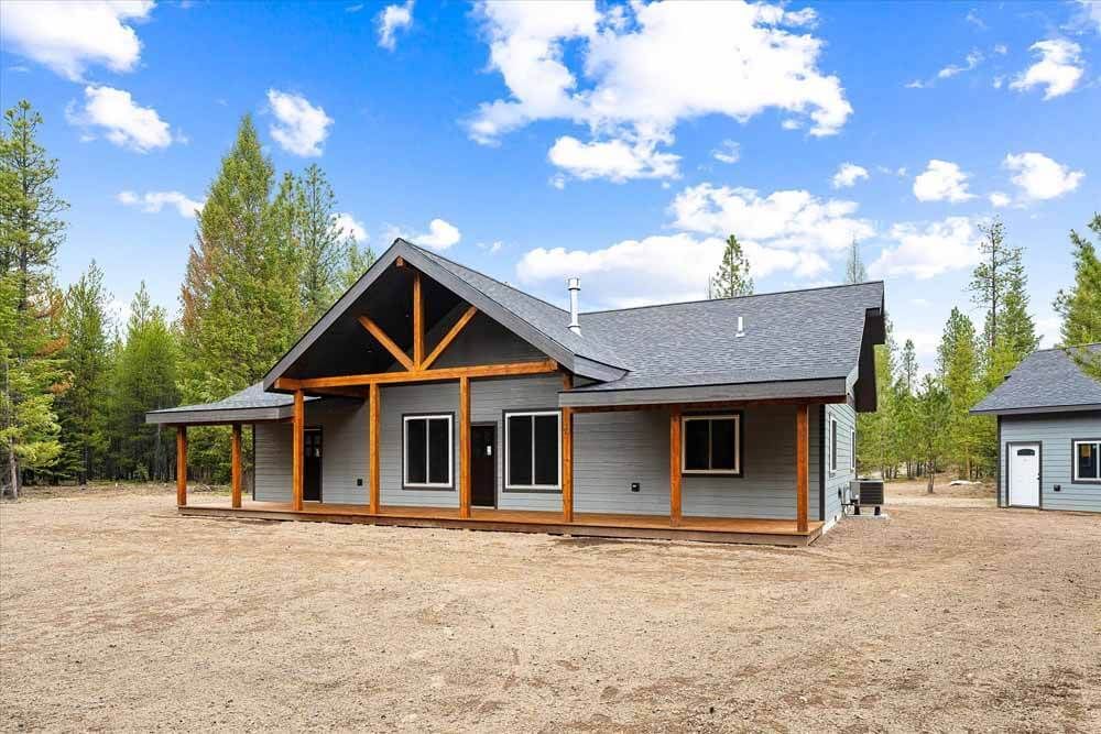 A house with a porch is sitting in the middle of a dirt field.