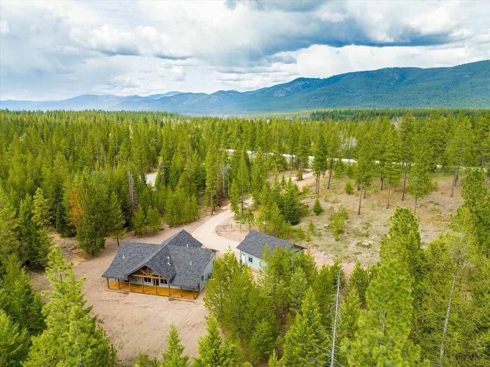 An aerial view of a house in the middle of a forest with mountains.