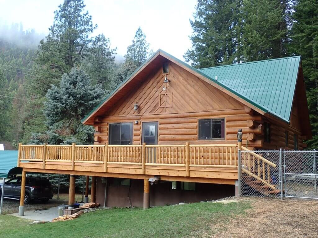 A log cabin with a green roof and a large deck