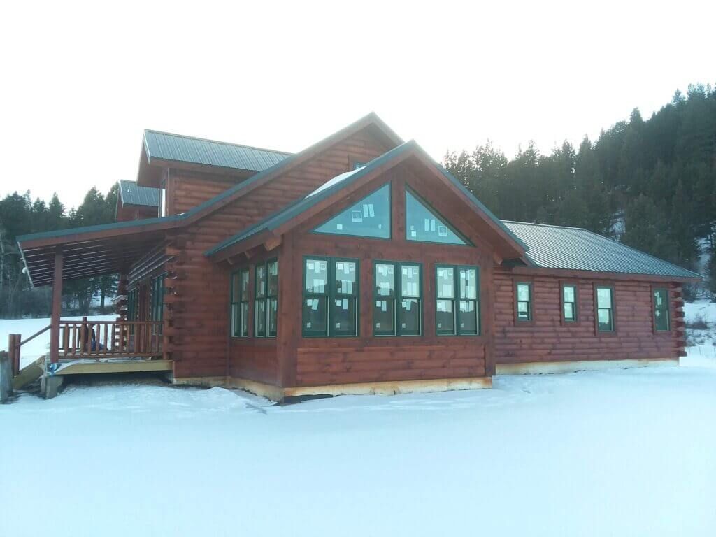A large log cabin is sitting in the middle of a snow covered field.