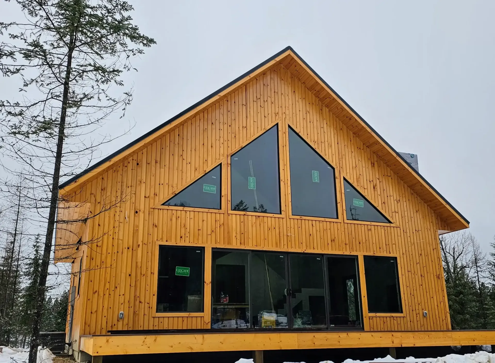 A large wooden house with a lot of windows is surrounded by snow.