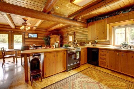 A kitchen in a log cabin with wooden cabinets and a rug on the floor.