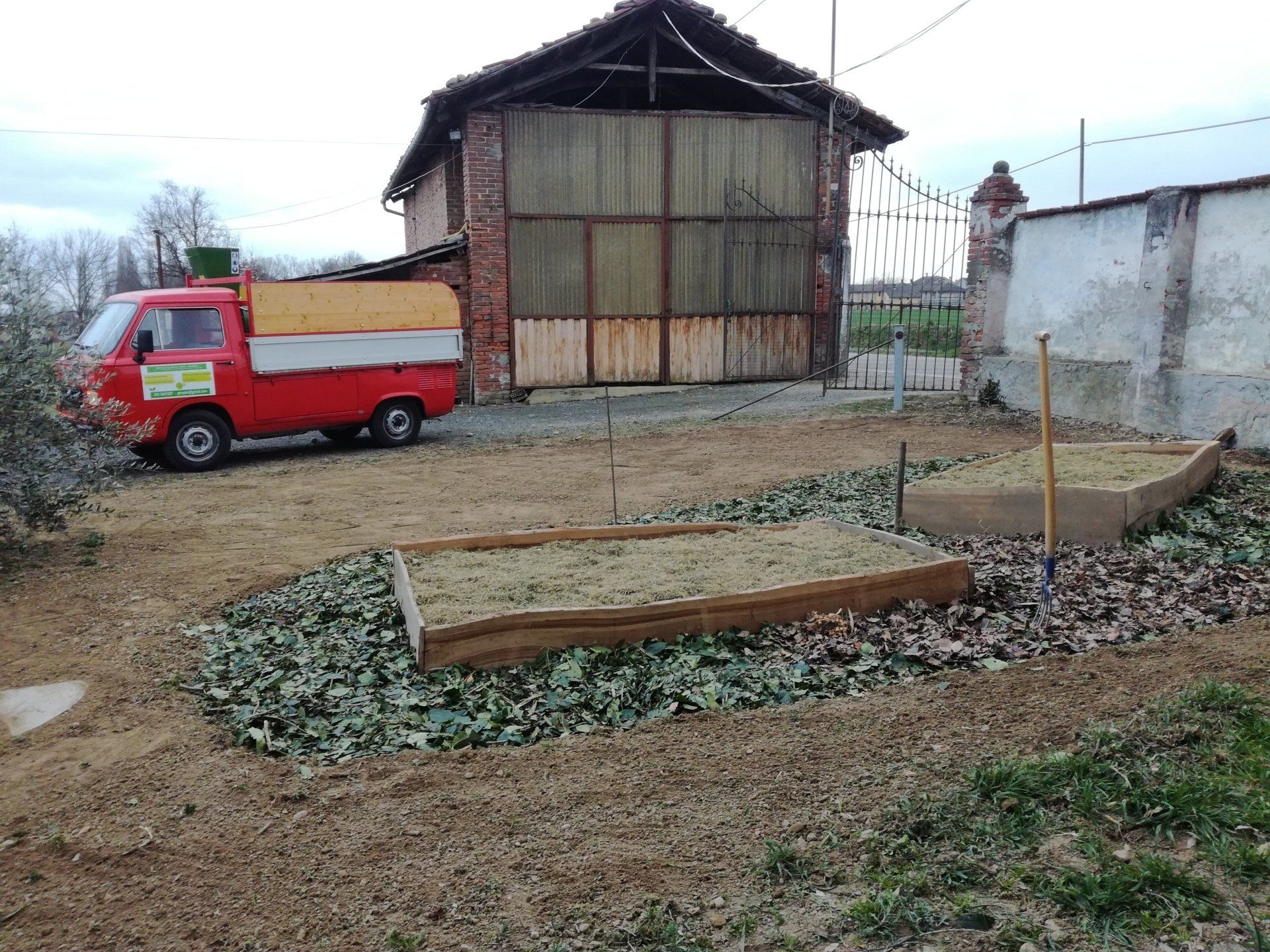 Un camion rosso accanto a due aiuole rialzate di fronte a un edificio in mattoni con un grande cancello.