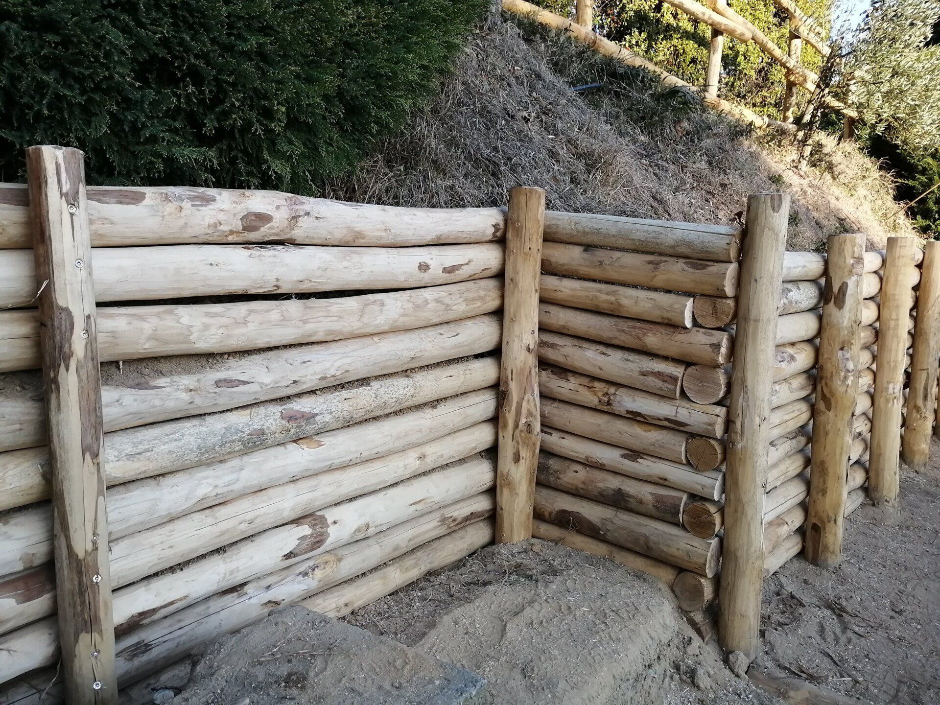 Muro di contenimento in tronchi di legno accanto a un terrapieno.
