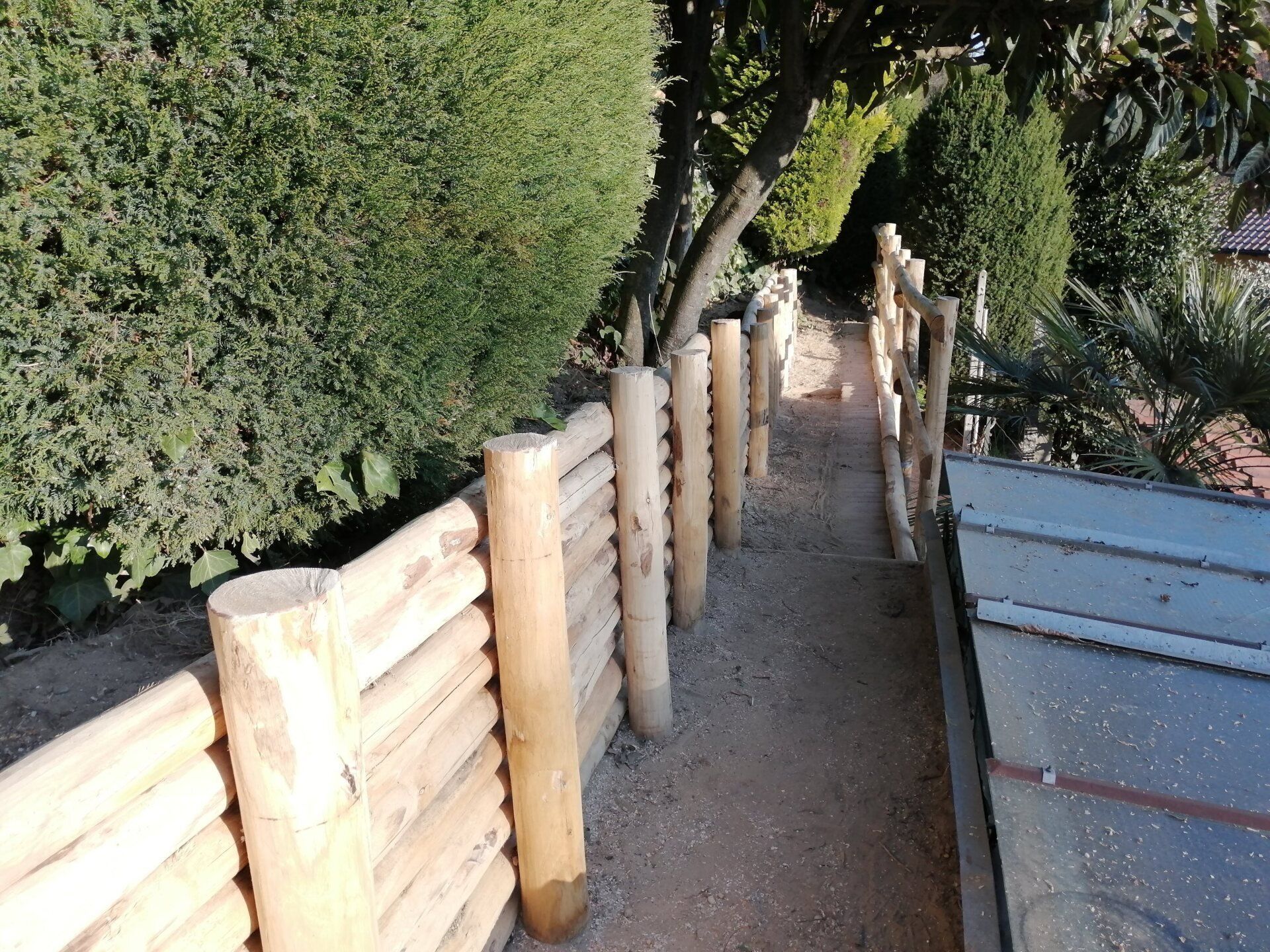 Una recinzione di tronchi costeggia un sentiero di ghiaia, con fogliame verde sopra.