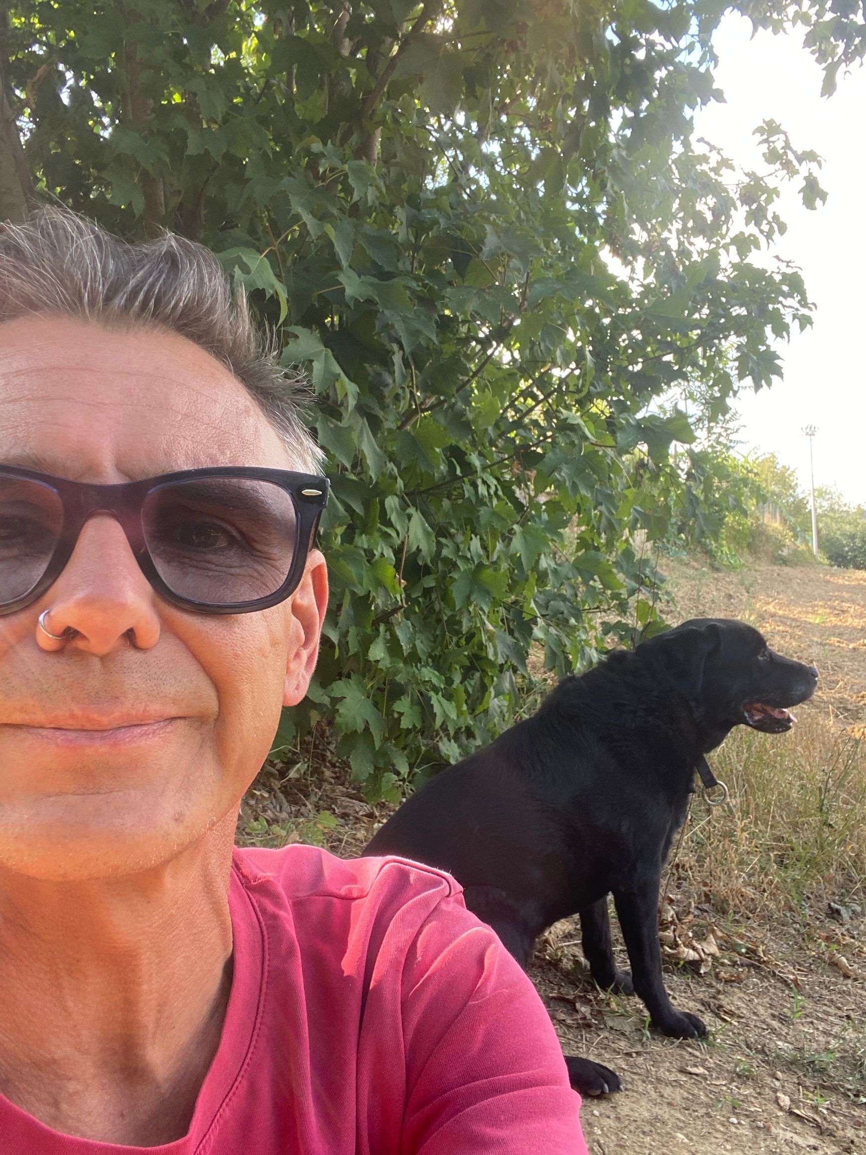 Uomo con occhiali e sciarpa davanti a un albero, illuminato dal sole.