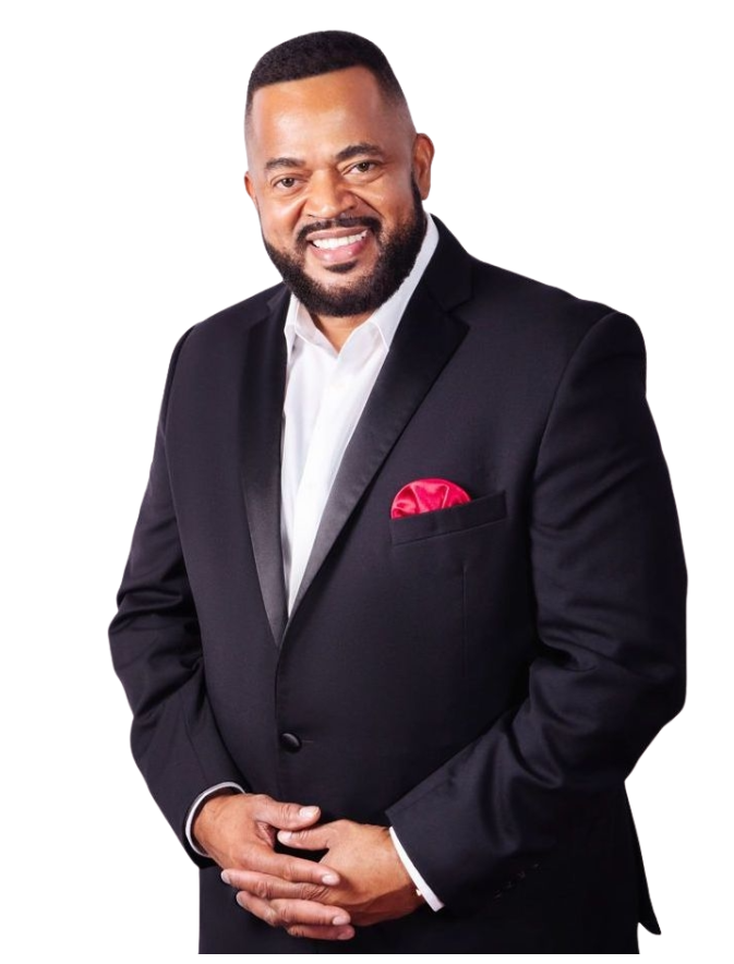 A man in a tuxedo with a red pocket square is smiling.