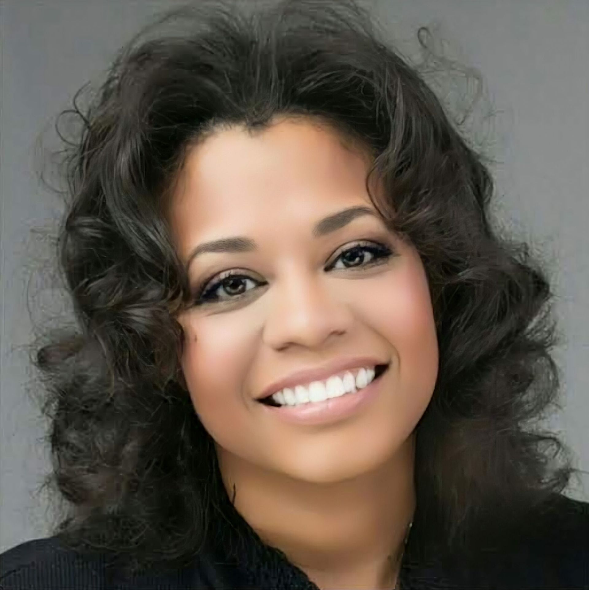 Woman with curly dark hair smiles, looking at the camera.