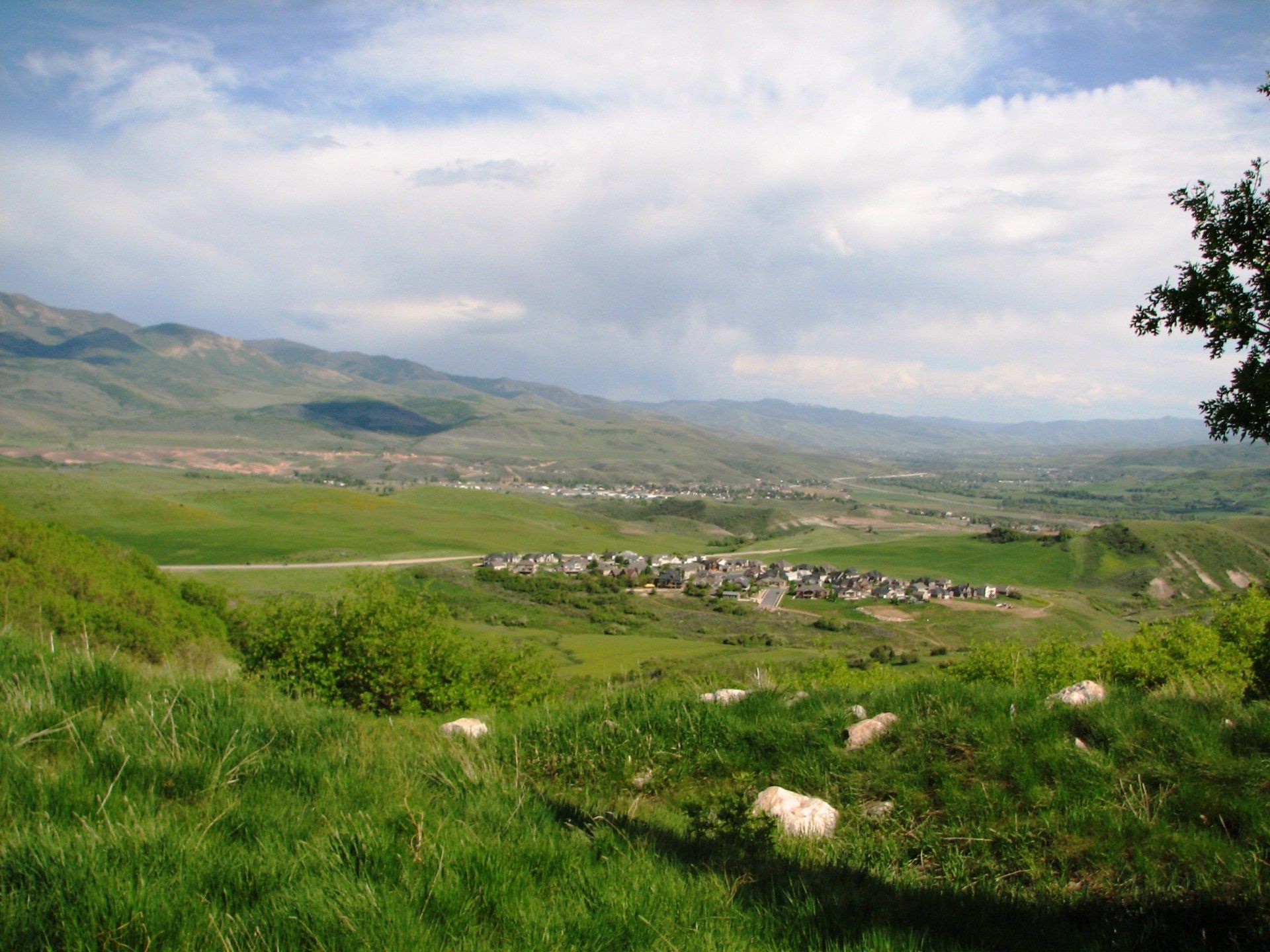 Green valley with a village and mountains under a cloudy sky.